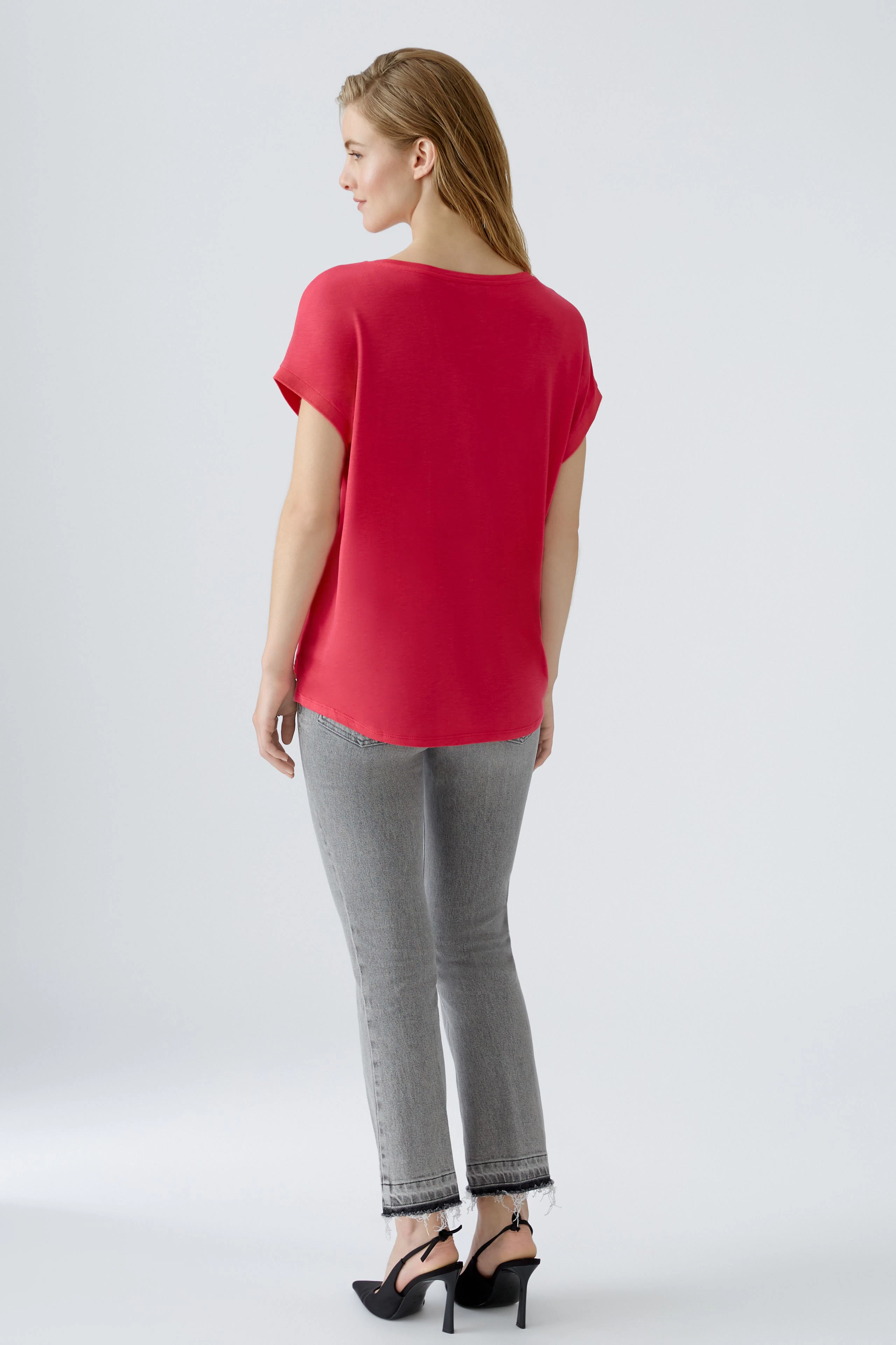 Bequemes Blusenshirt: Frau in rotem Shirt mit lässigem Schnitt und grauen Jeans, von hinten zu sehen.