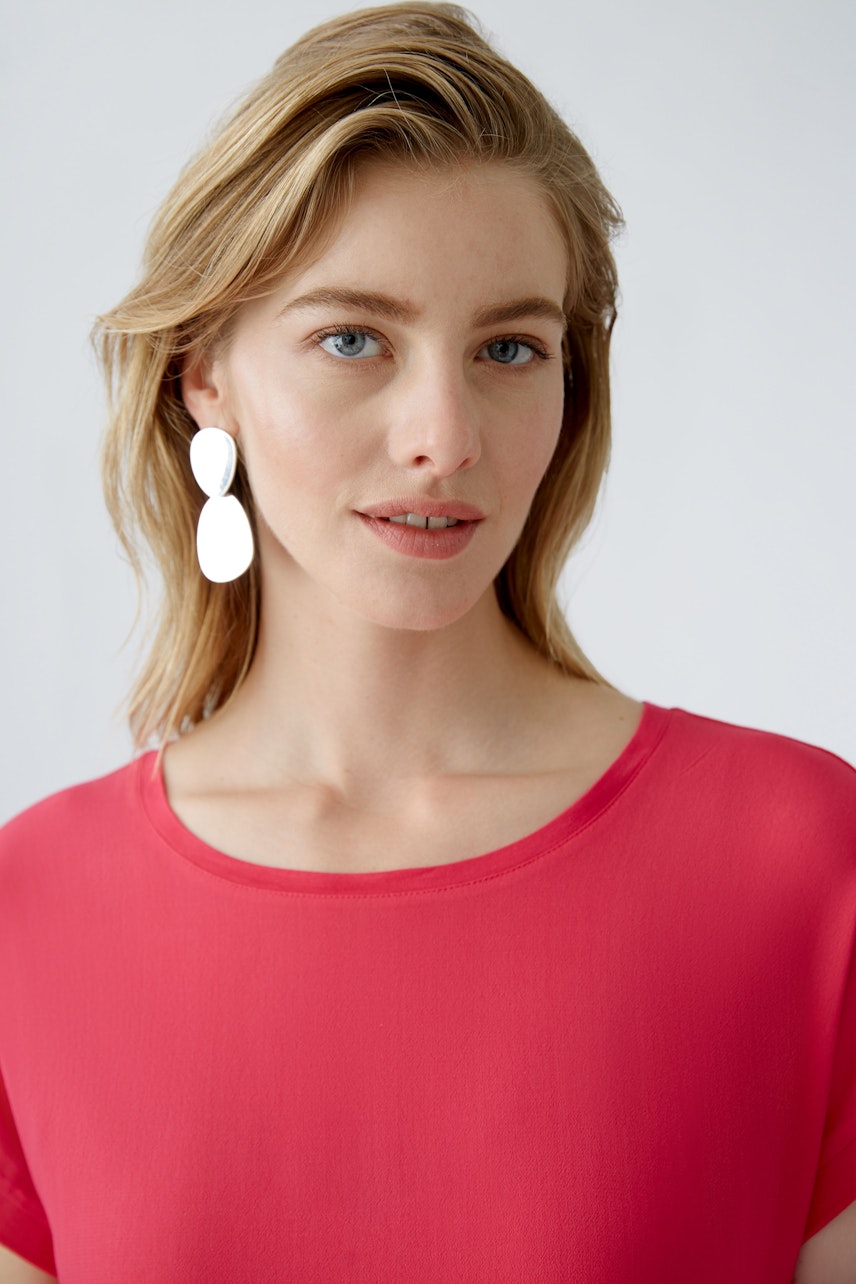 Stylish blouse shirt: Woman in a vibrant pink top with a relaxed fit and elegant earrings.