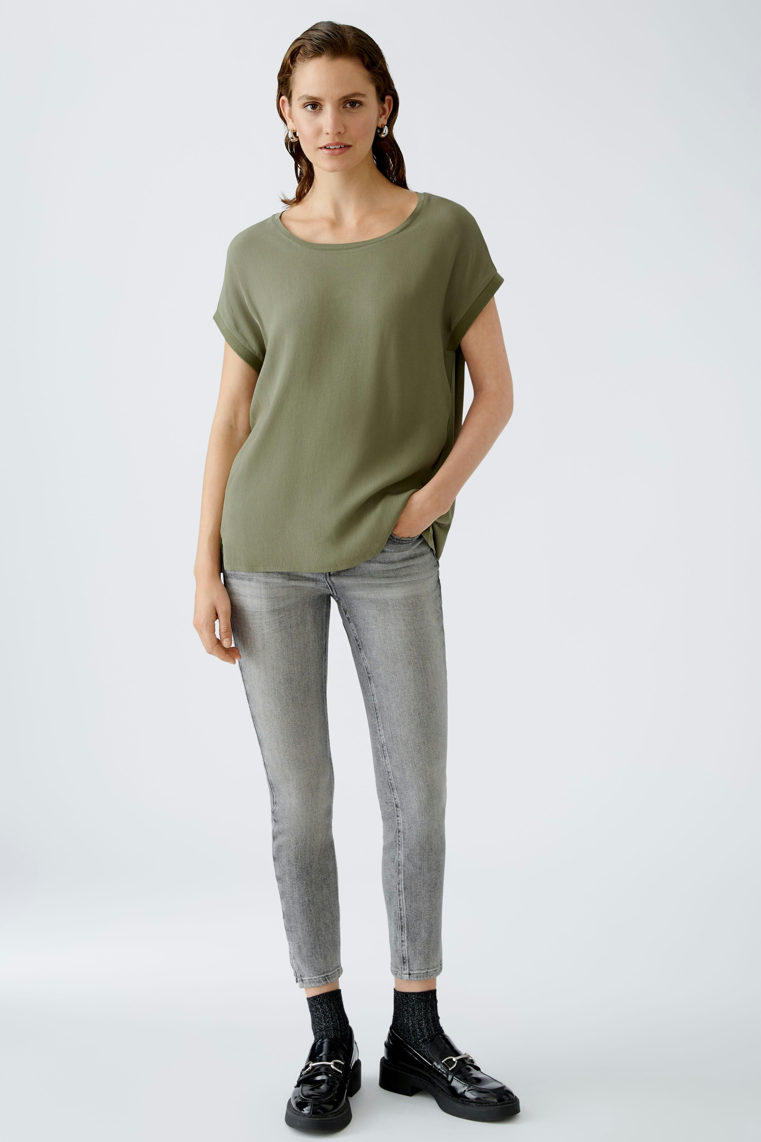 Casual women's blouse shirt: A woman in a loose olive green top paired with gray jeans.
