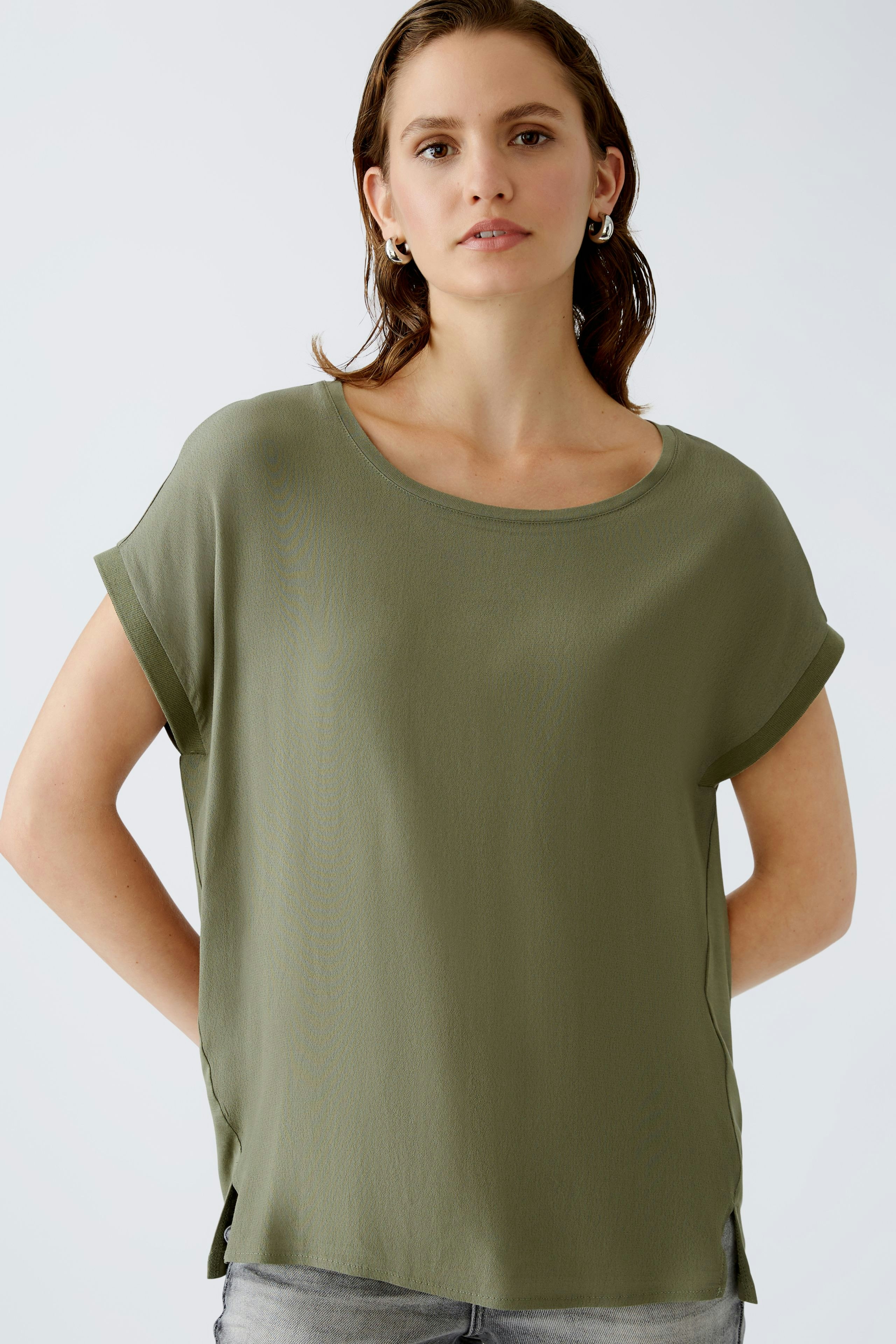 Casual women's blouse shirt: A woman in a relaxed olive green top with rolled sleeves and side slits.