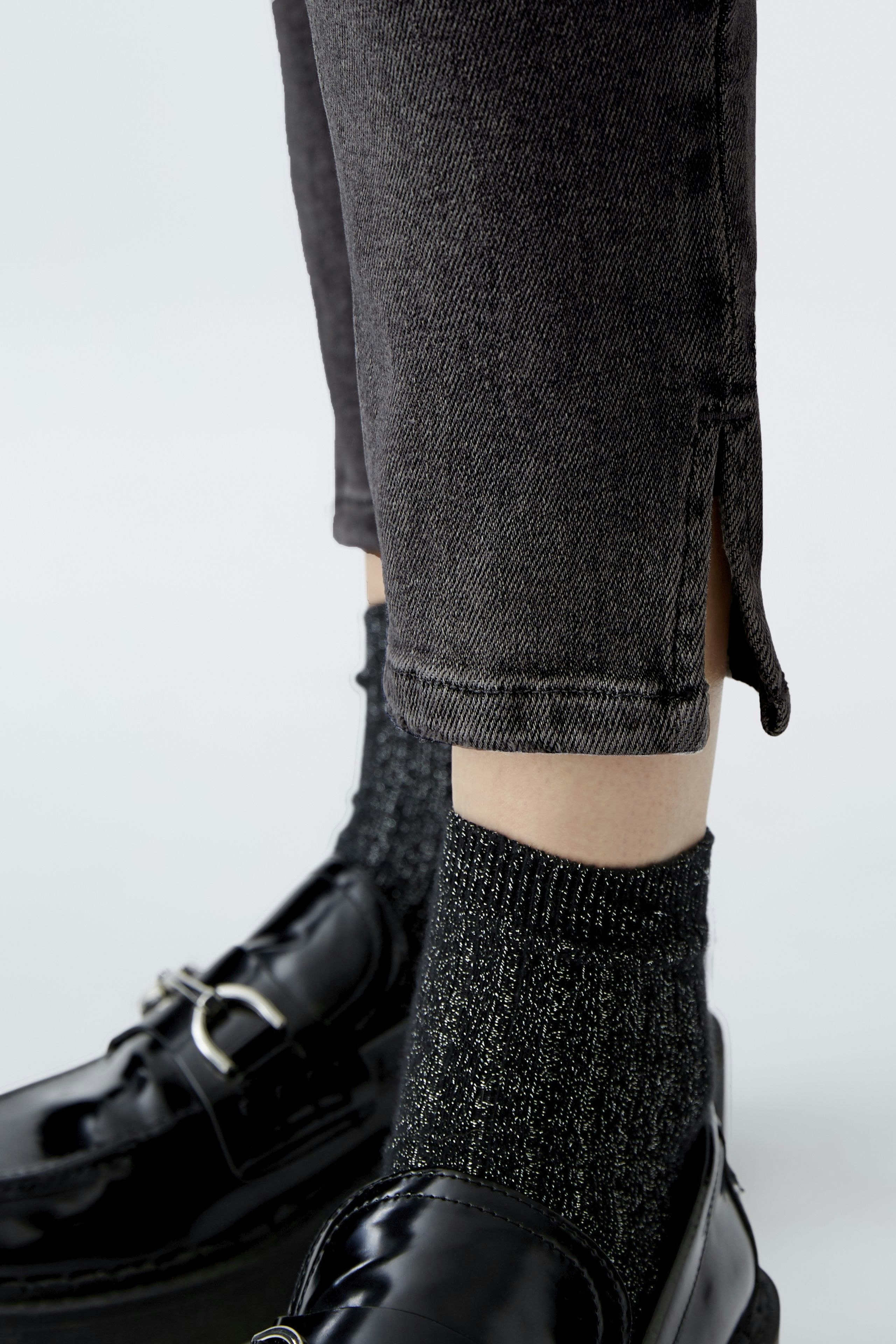 Stylish skinny jeans: A woman showcases dark jeans with a modern cut and unique side slits.