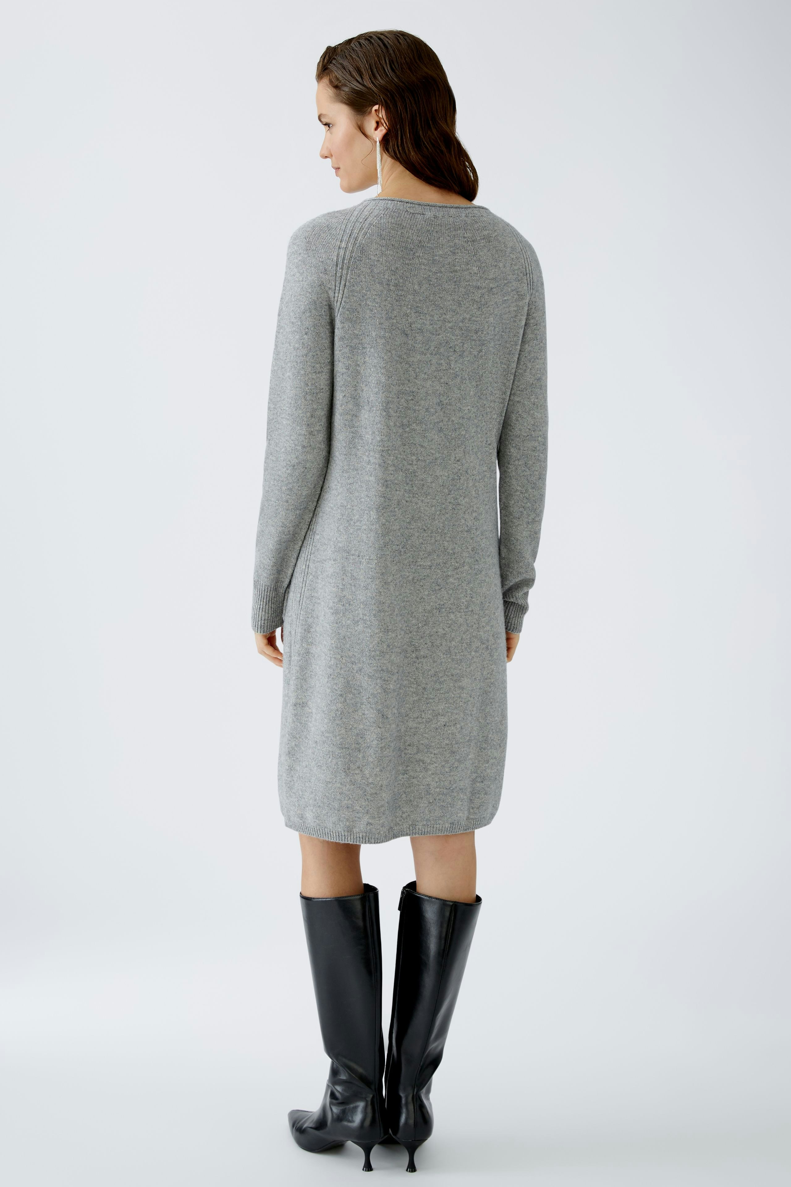 Elegantes Damen-Kleid: Frau in grauem, langärmligem Kleid mit schlichten Linien und modischen Stiefeln.