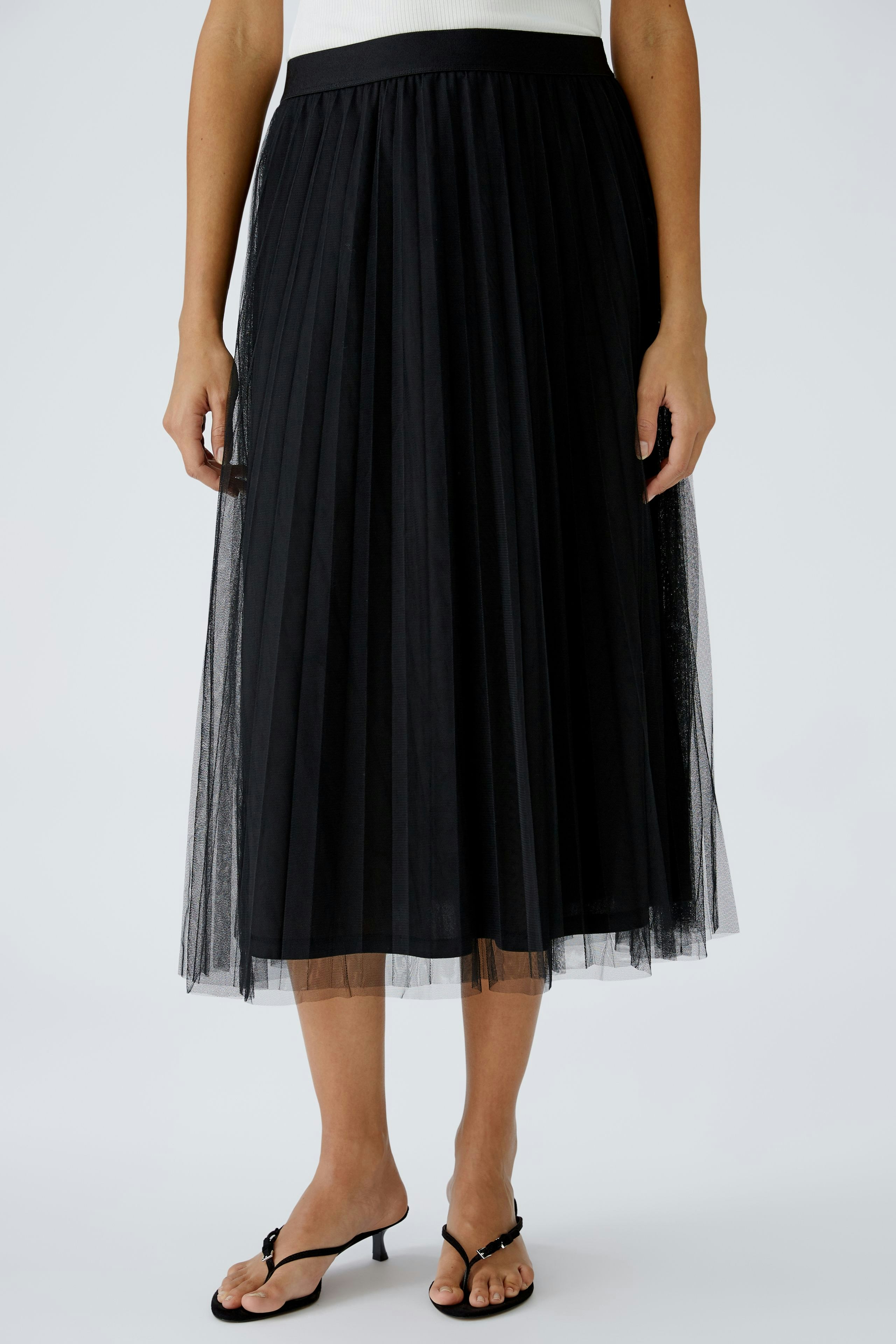 Elegant midi skirt: Woman in a black pleated skirt with a tulle overlay, perfect for any occasion.