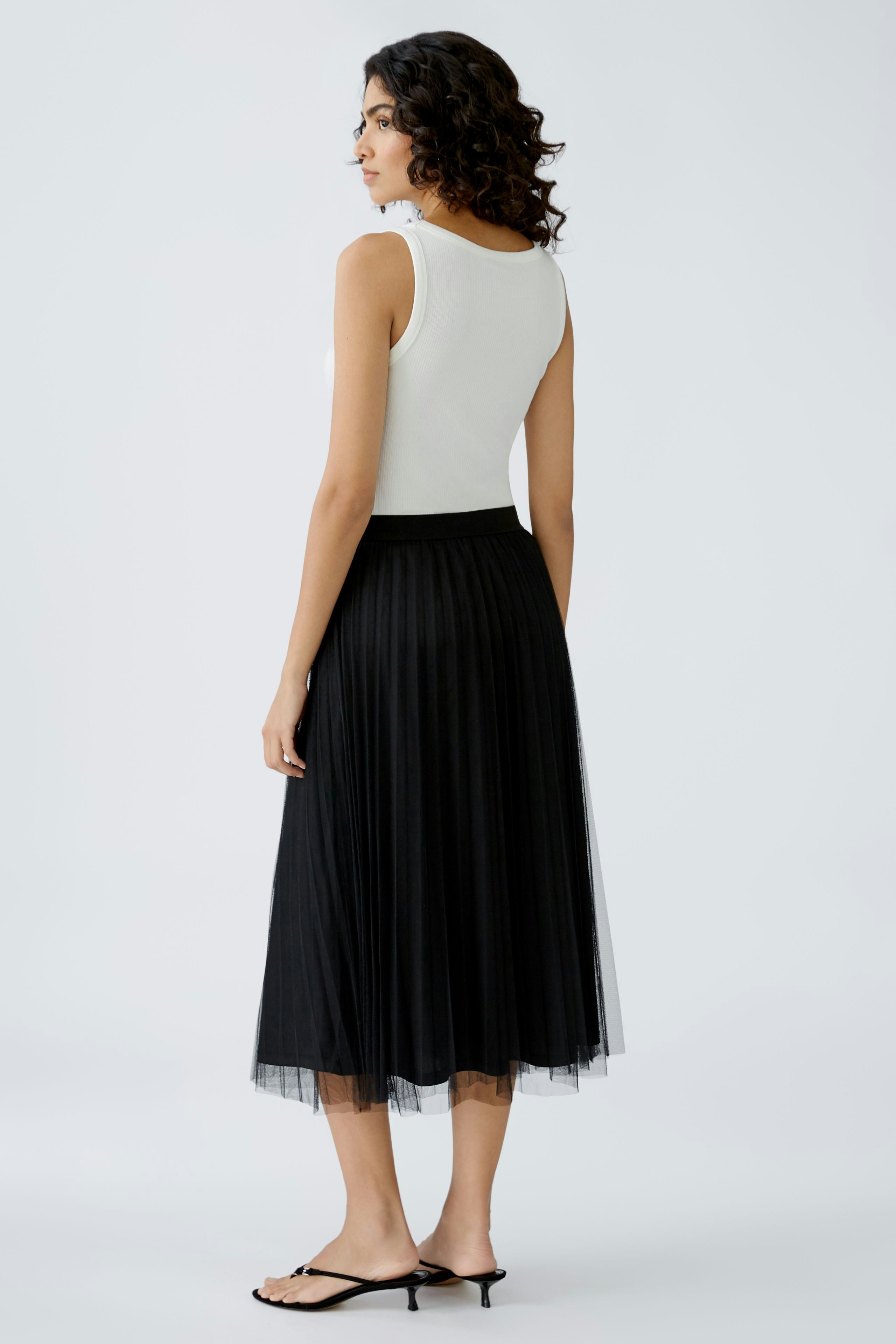 Elegant midi skirt: Woman in a black pleated midi skirt, showcasing a stylish and versatile look.