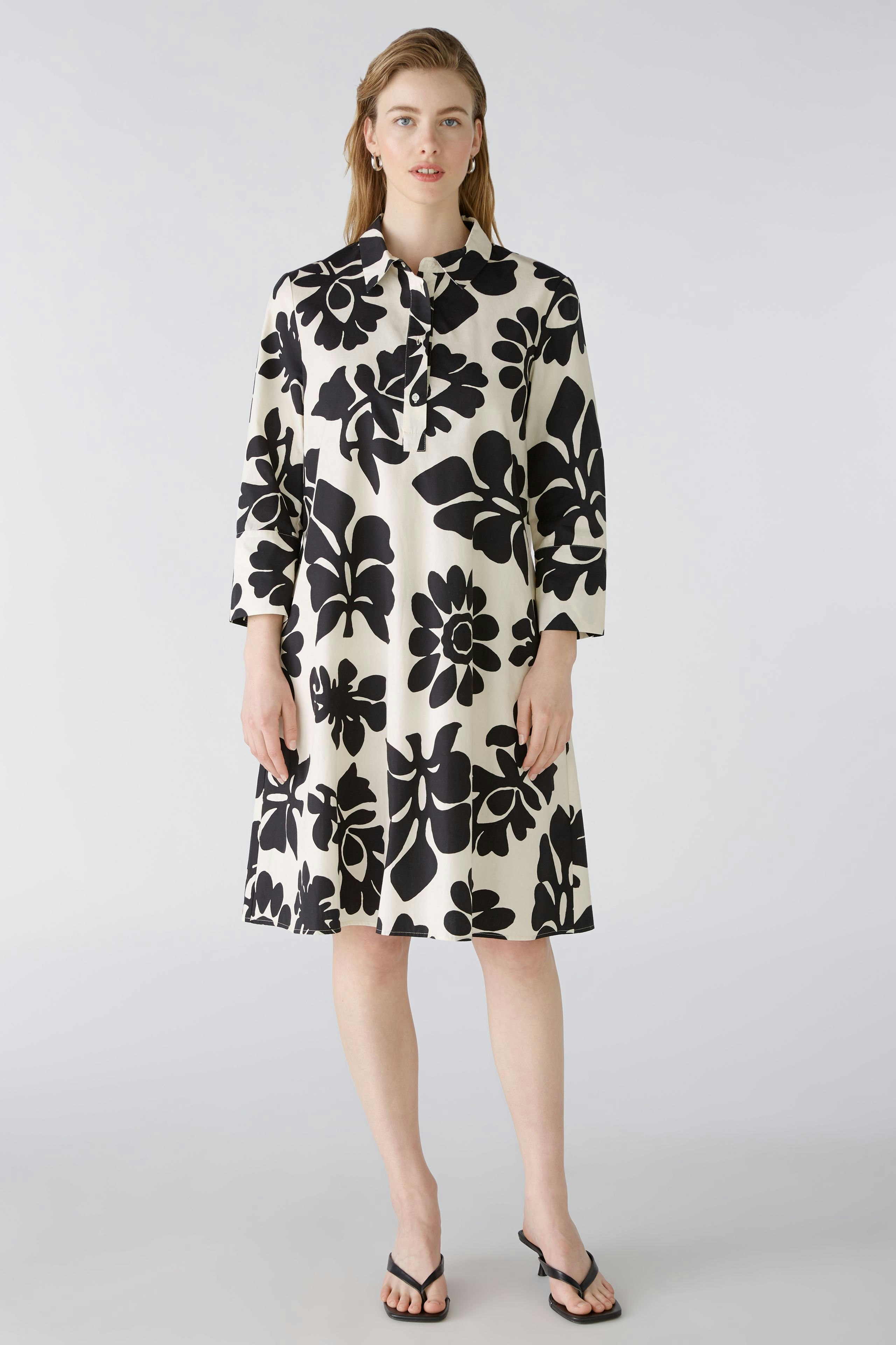 Stylish dress: A woman in a floral-patterned dress with a collar stands confidently.
