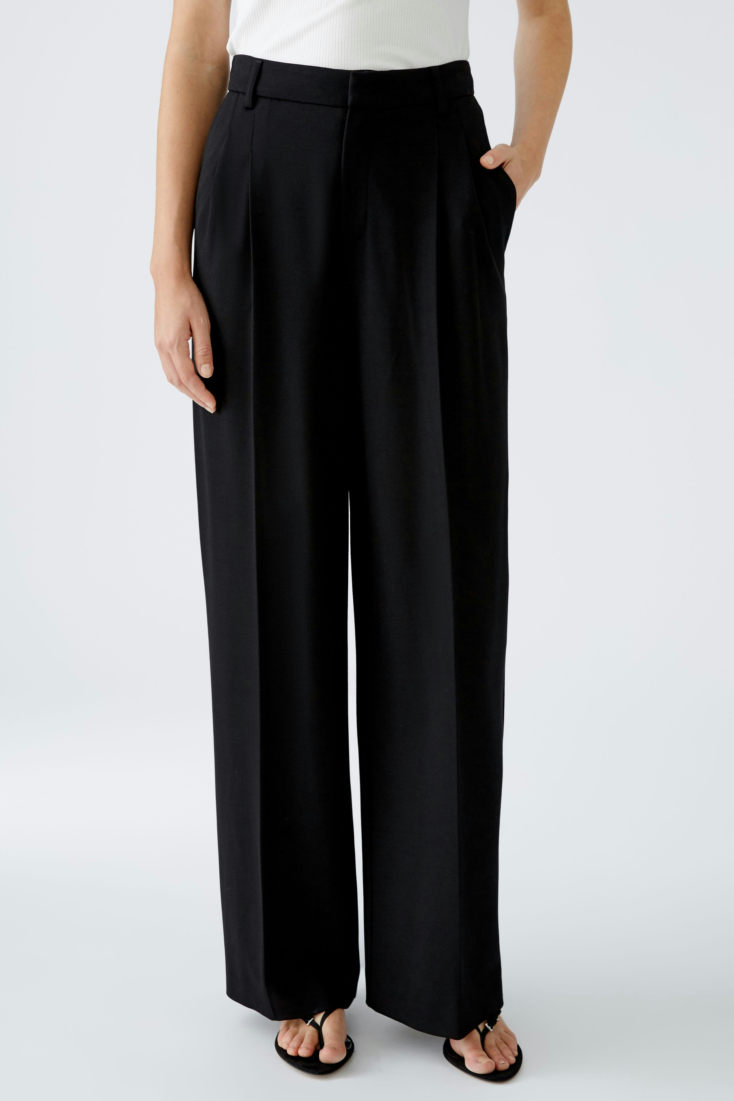 Elegant women's pleated trousers: A woman in black trousers with a relaxed fit stands confidently.