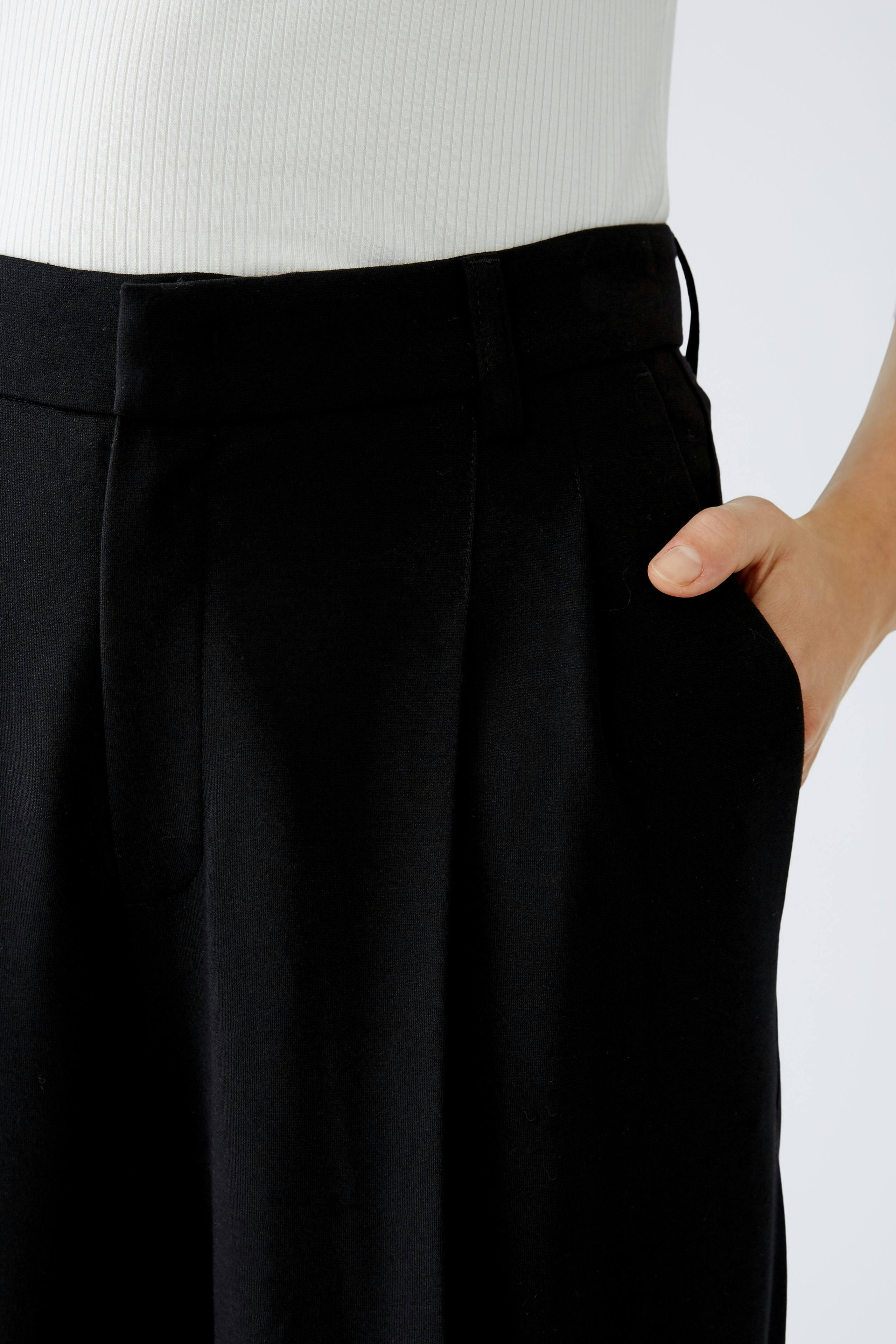 Elegant women's pleated trousers: A woman in stylish black trousers with a relaxed fit.