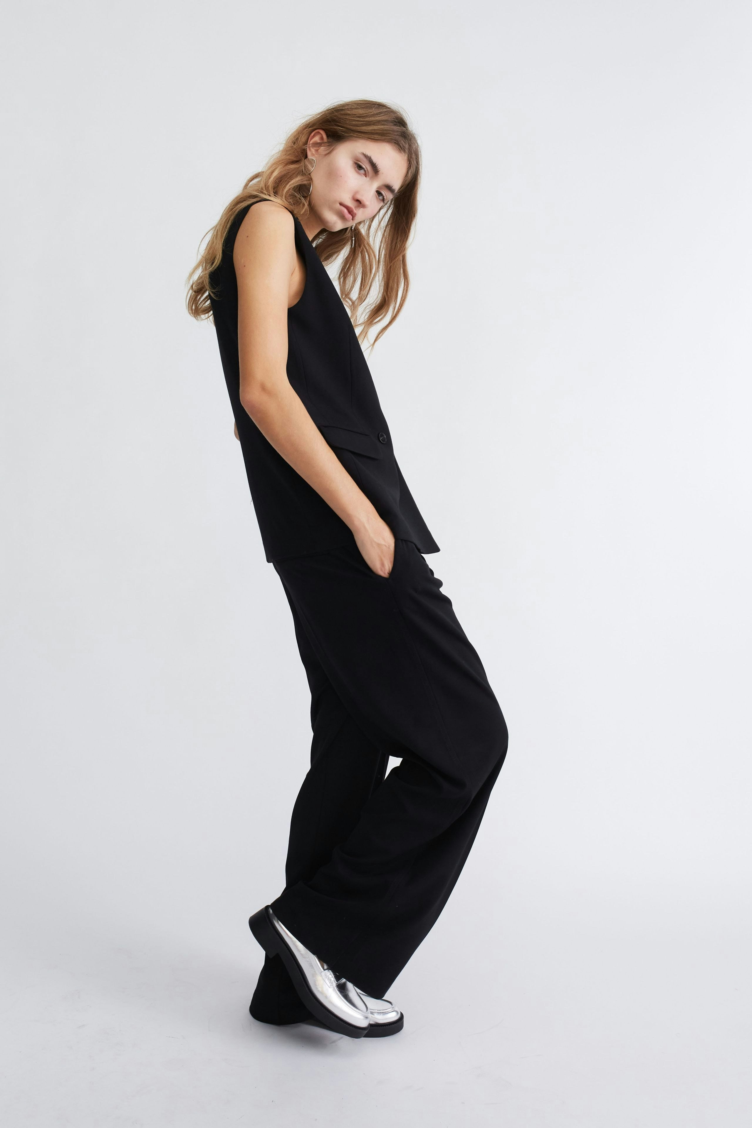 Elegant women's pleated trousers: A woman poses confidently in stylish black trousers, showcasing modern fashion.