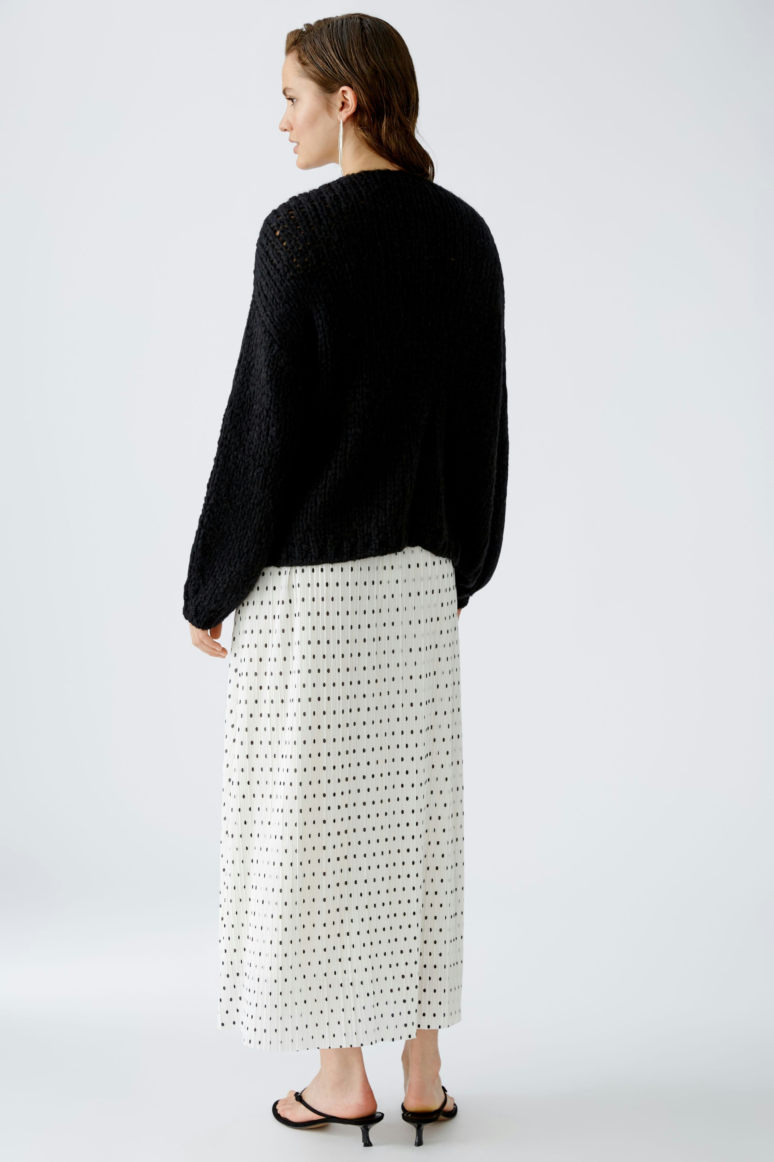 Schwarze Strickjacke: Frau mit lässiger Strickjacke und langem, gepunktetem Rock steht entspannt.