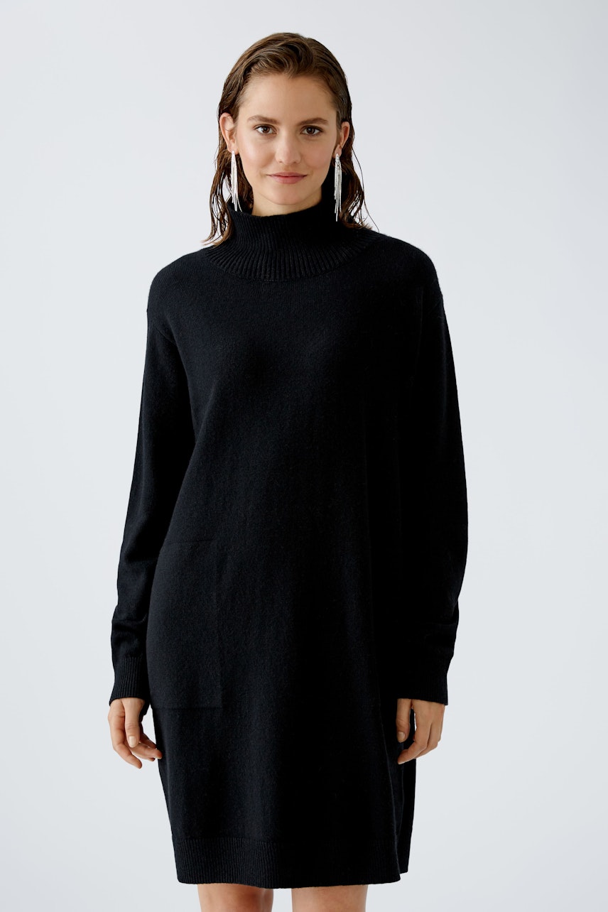 Elegant women's dress: A woman in a black turtleneck dress with long sleeves stands confidently.