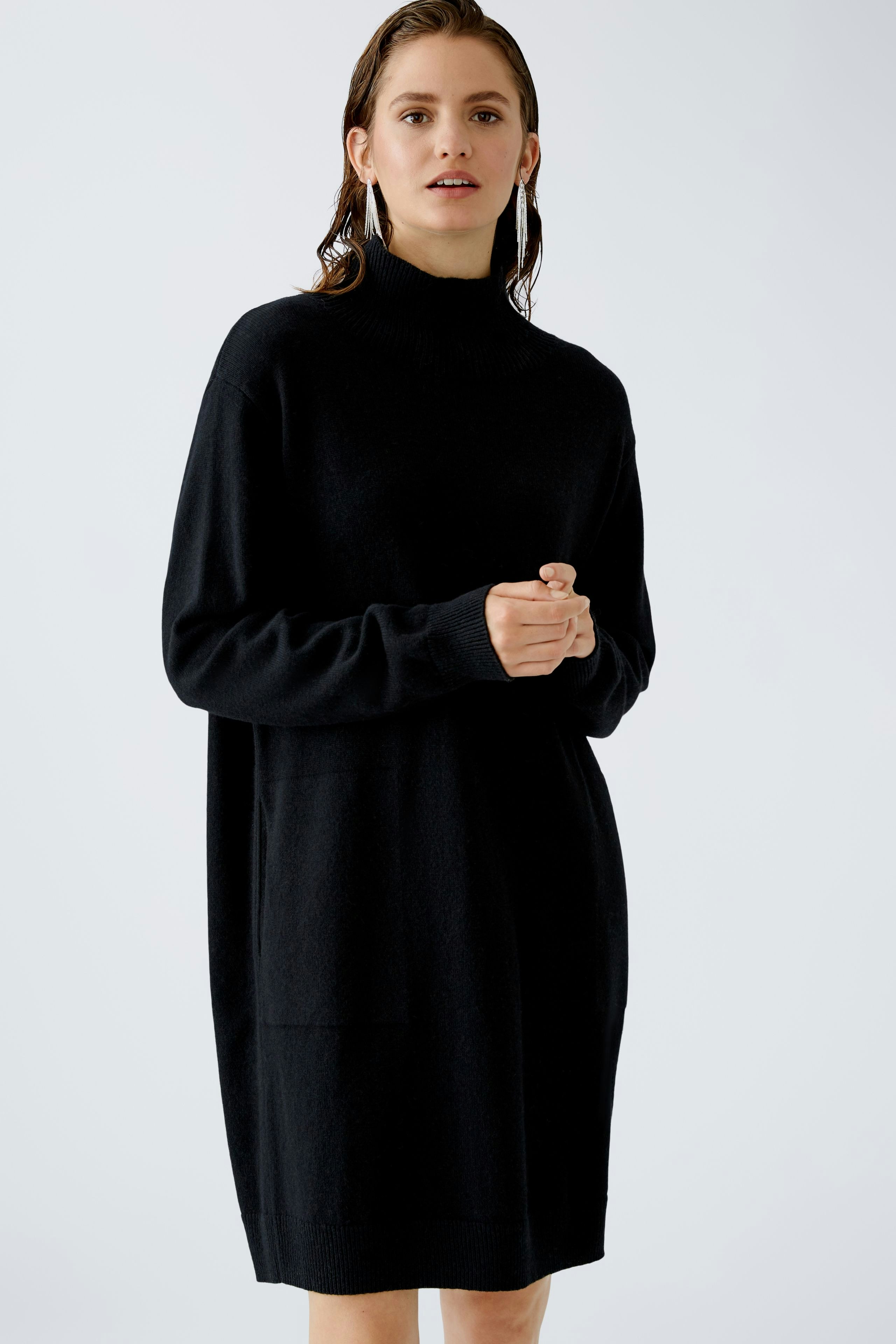 Elegant women's dress: A woman in a black dress with a high neck and relaxed fit stands confidently.