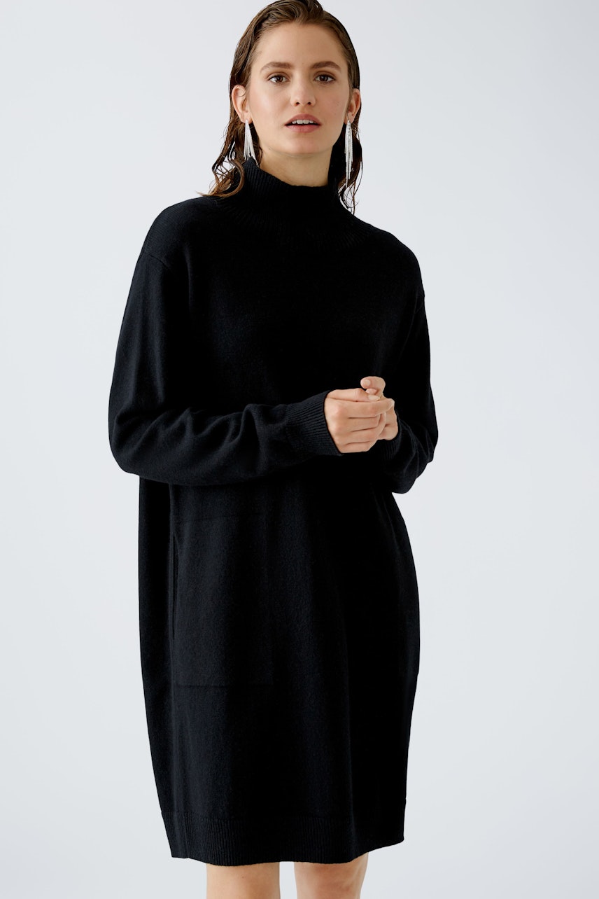 Elegant women's dress: A woman in a black dress with a high neck and relaxed fit stands confidently.