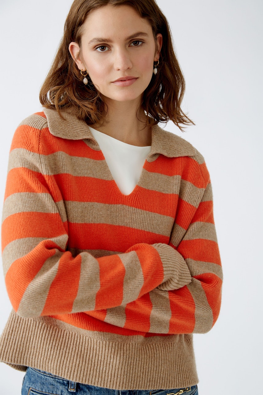 This image features a woman wearing a stylish striped sweater, showcasing a vibrant combination of orange and beige stripes. The sweater has a cozy collar and a relaxed fit, perfect for casual outings or layering during cooler days. She pairs it with classic denim, creating a chic and comfortable look. This outfit is ideal for those looking to add a pop of color to their wardrobe while maintaining a laid-back style.