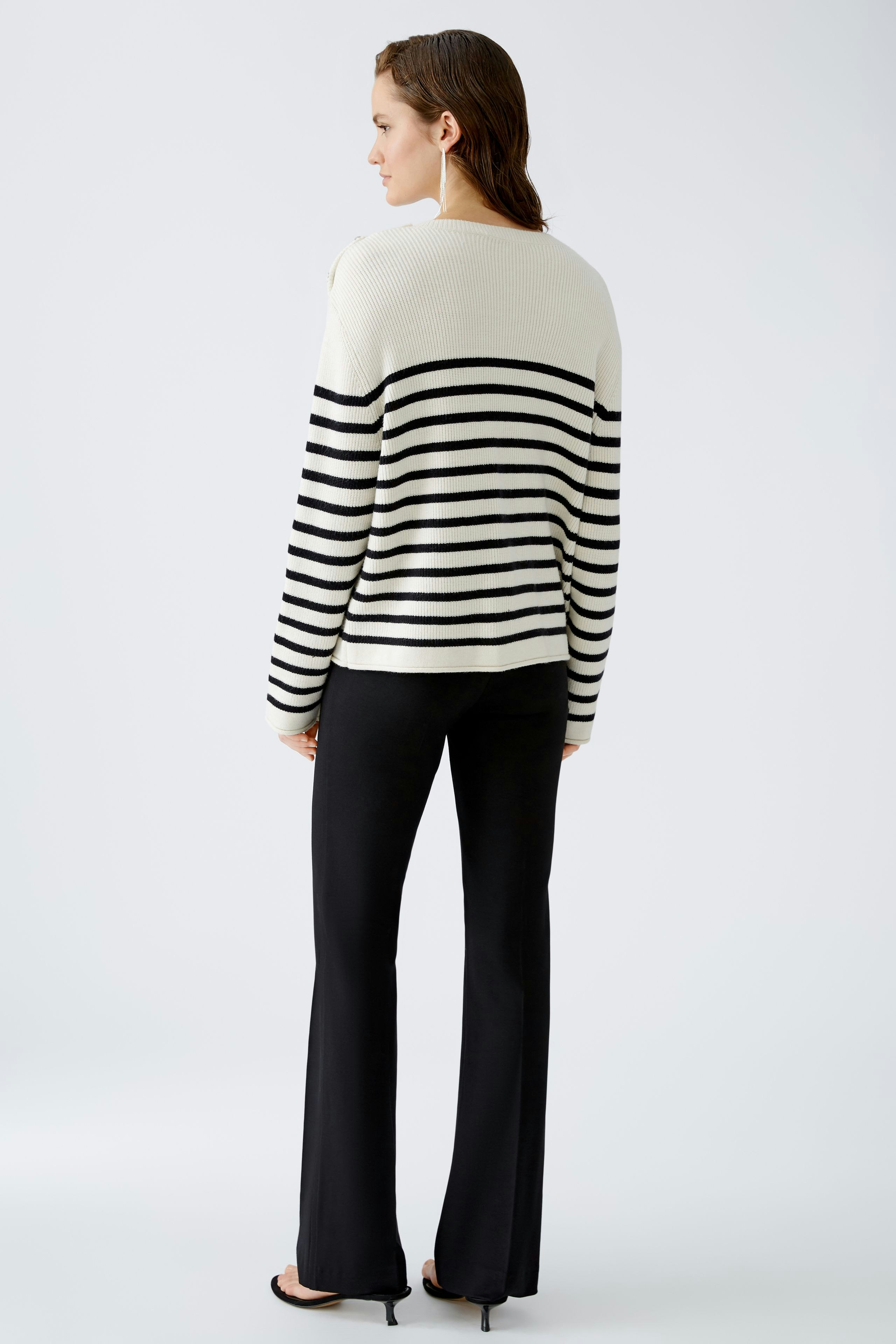 Damen-Pullover: Frau trägt einen gestreiften Pullover in Schwarz und Weiß, kombiniert mit eleganten Hosen.