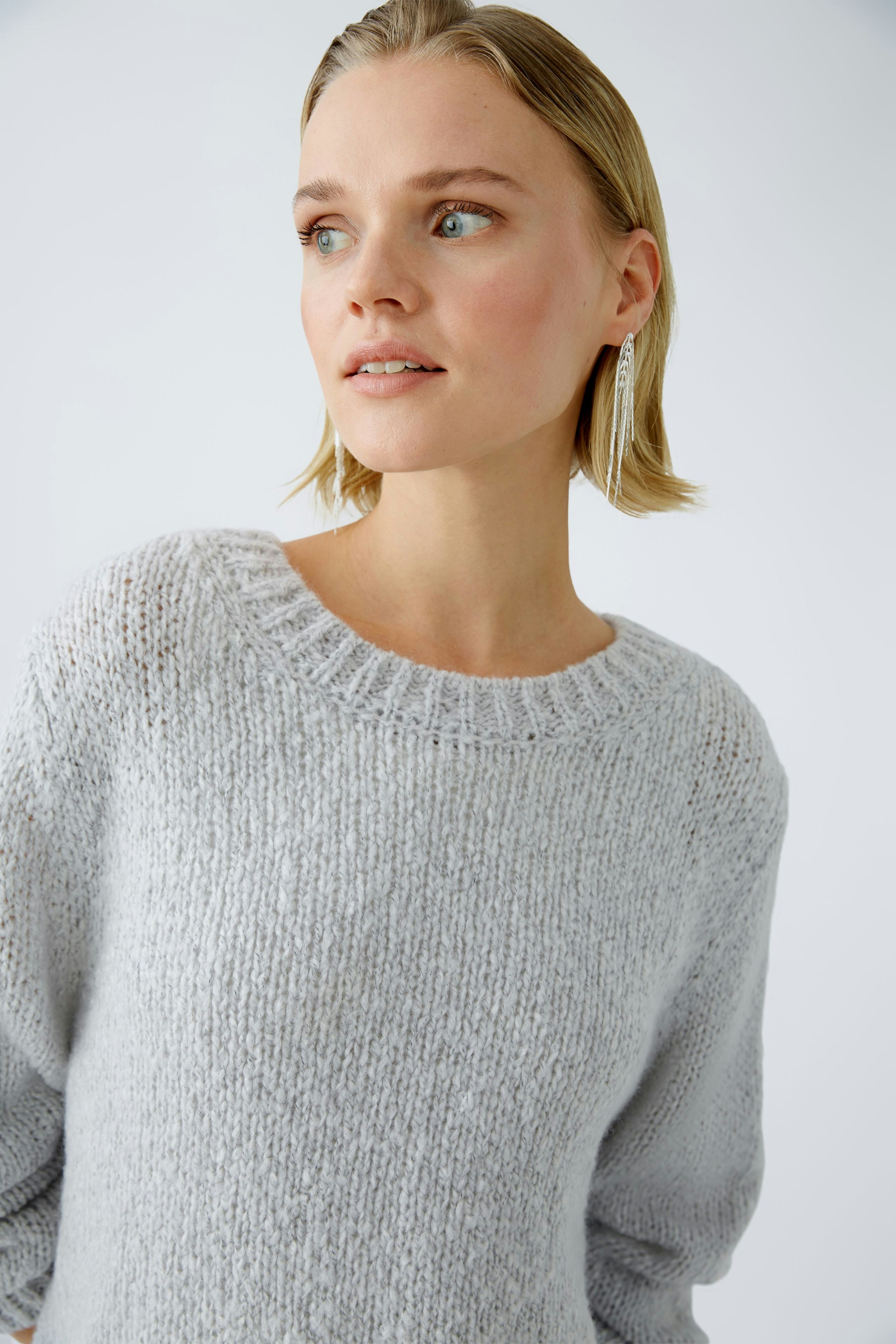 Modern women's pullover: A woman in a light gray knitted pullover with a relaxed fit.