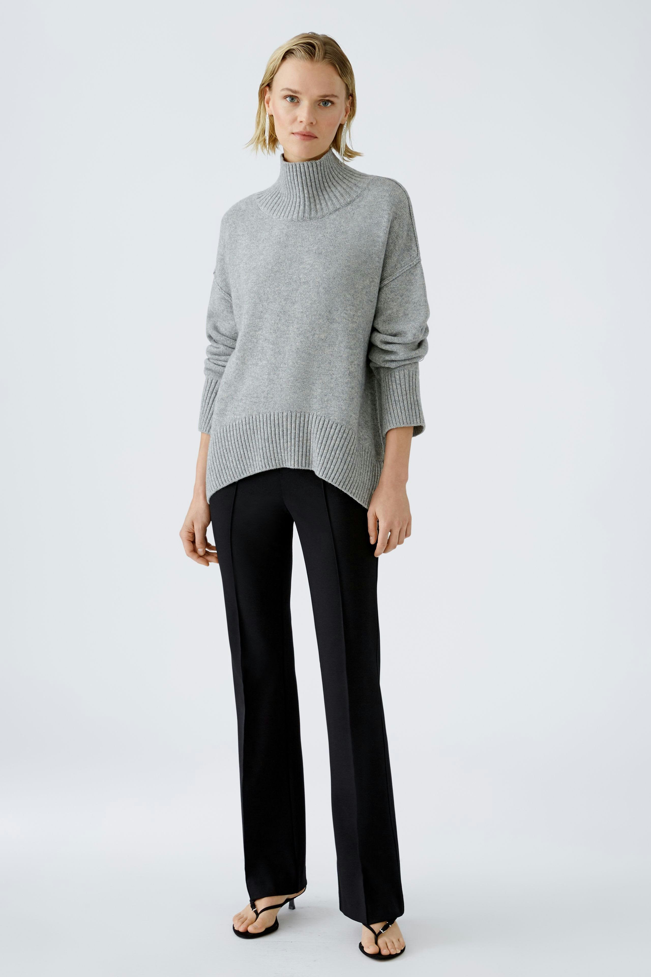 Modern women's pullover: A woman in a light gray turtleneck pullover paired with sleek black pants.