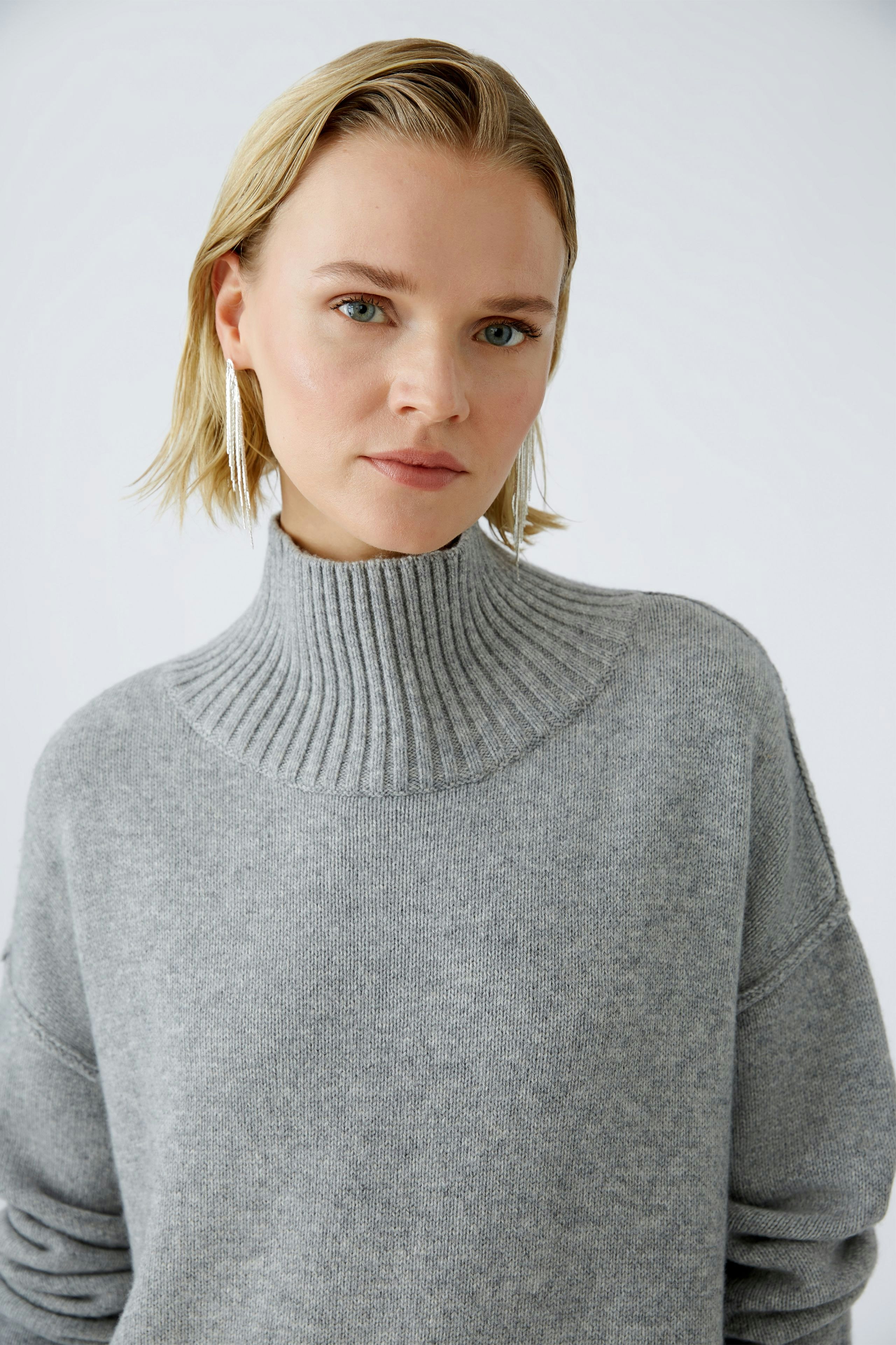 Modern women's pullover: A woman in a cozy gray pullover with a high collar looks confidently at the camera.