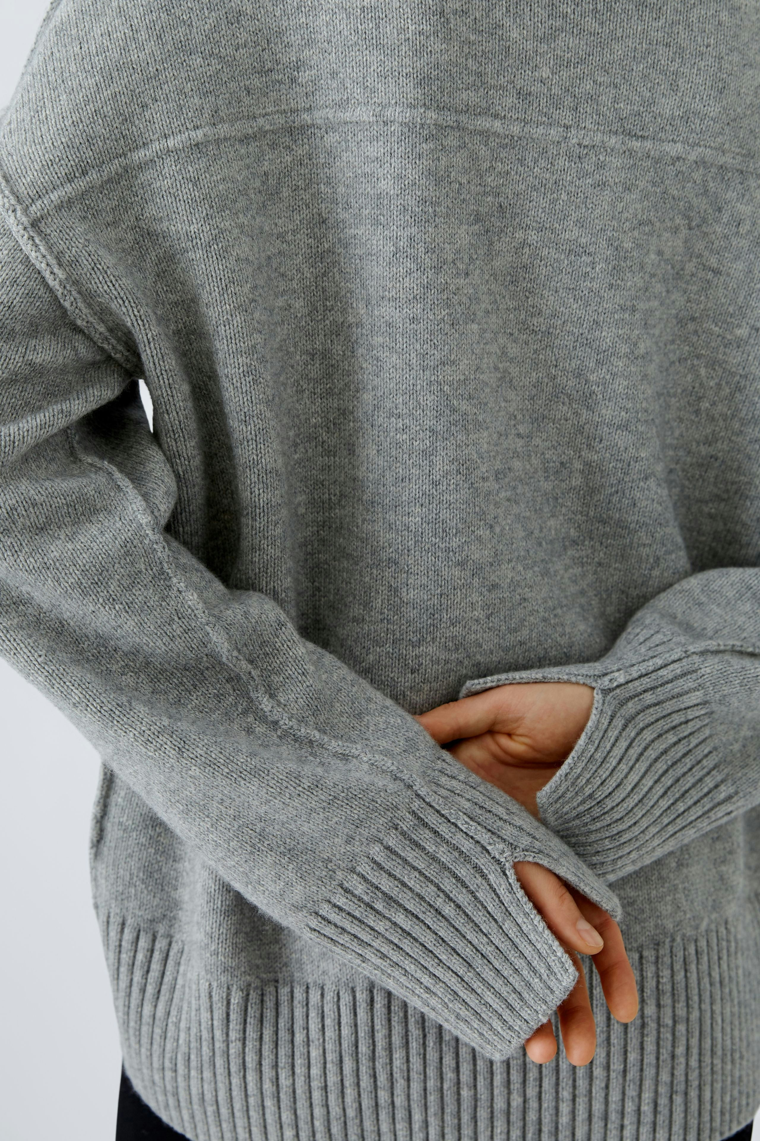 Stylish women's pullover: A woman in a cozy gray pullover with ribbed cuffs, hands clasped behind her.