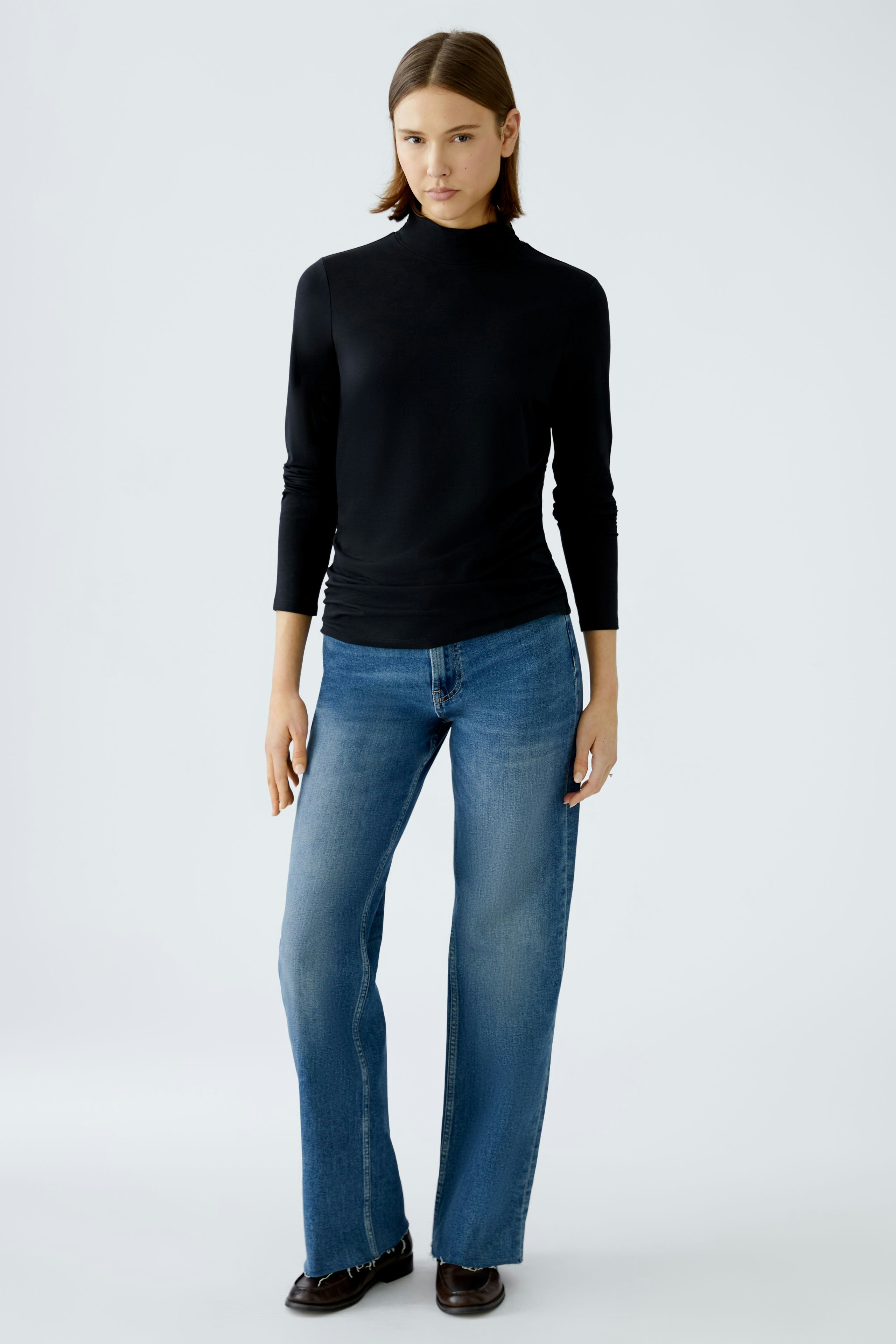 Elegantes Langarmshirt: Frau in schwarzem Shirt mit hohem Kragen und lässigen Jeans steht selbstbewusst.