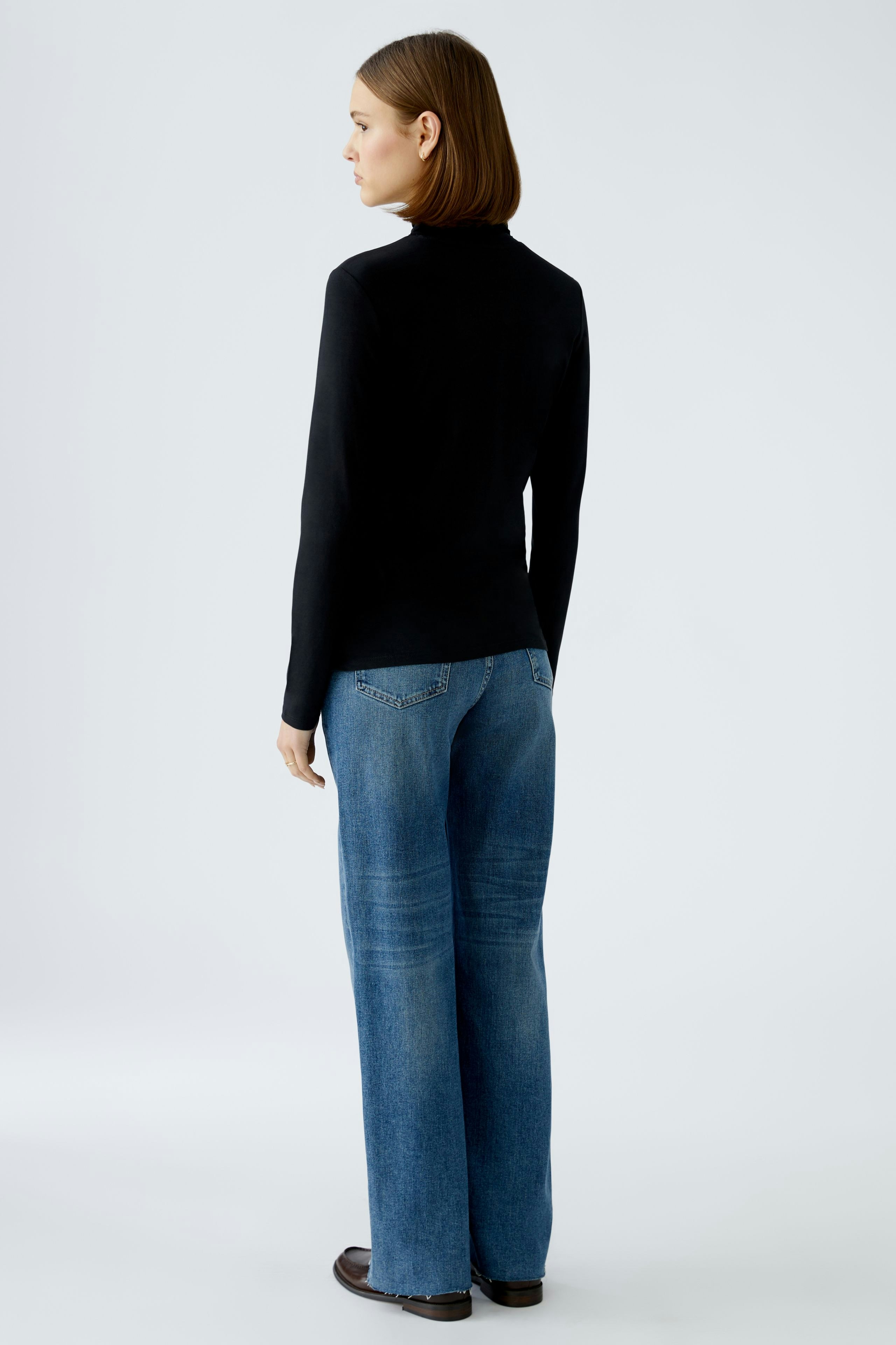 Elegantes Langarmshirt: Frau in schwarzem Shirt und lässigen Jeans zeigt einen modernen Look.