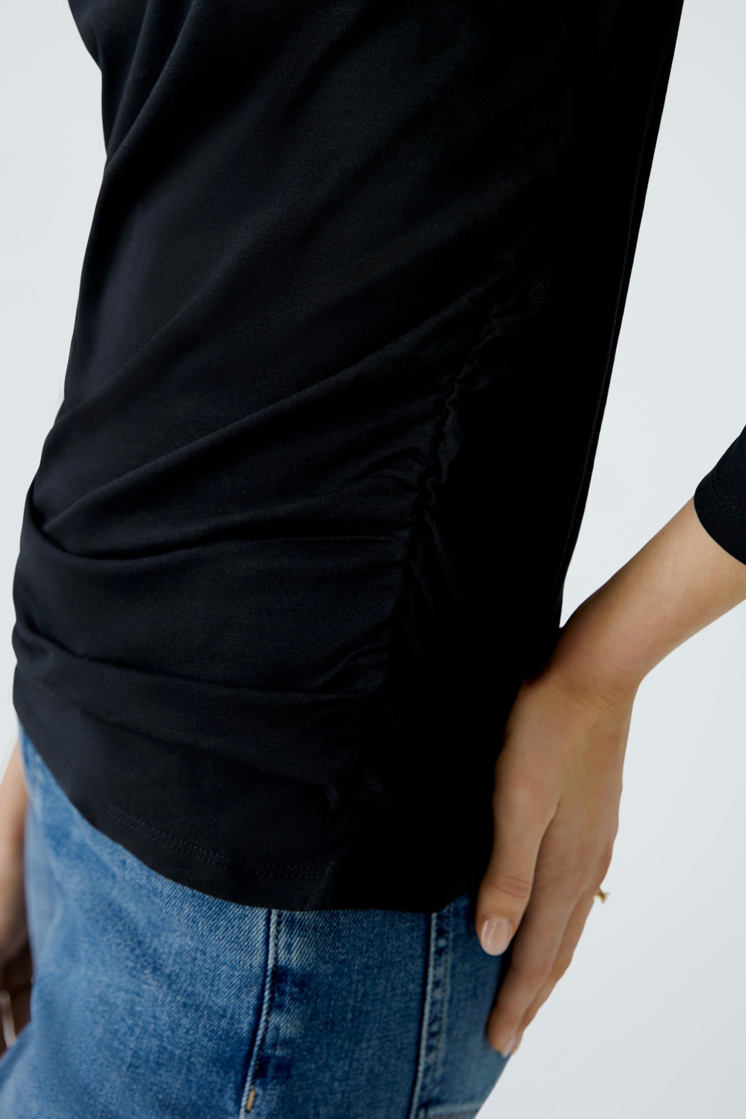 Elegantes Langarmshirt: Frau in schwarzem Shirt mit Raffung, kombiniert mit lässiger Jeans.