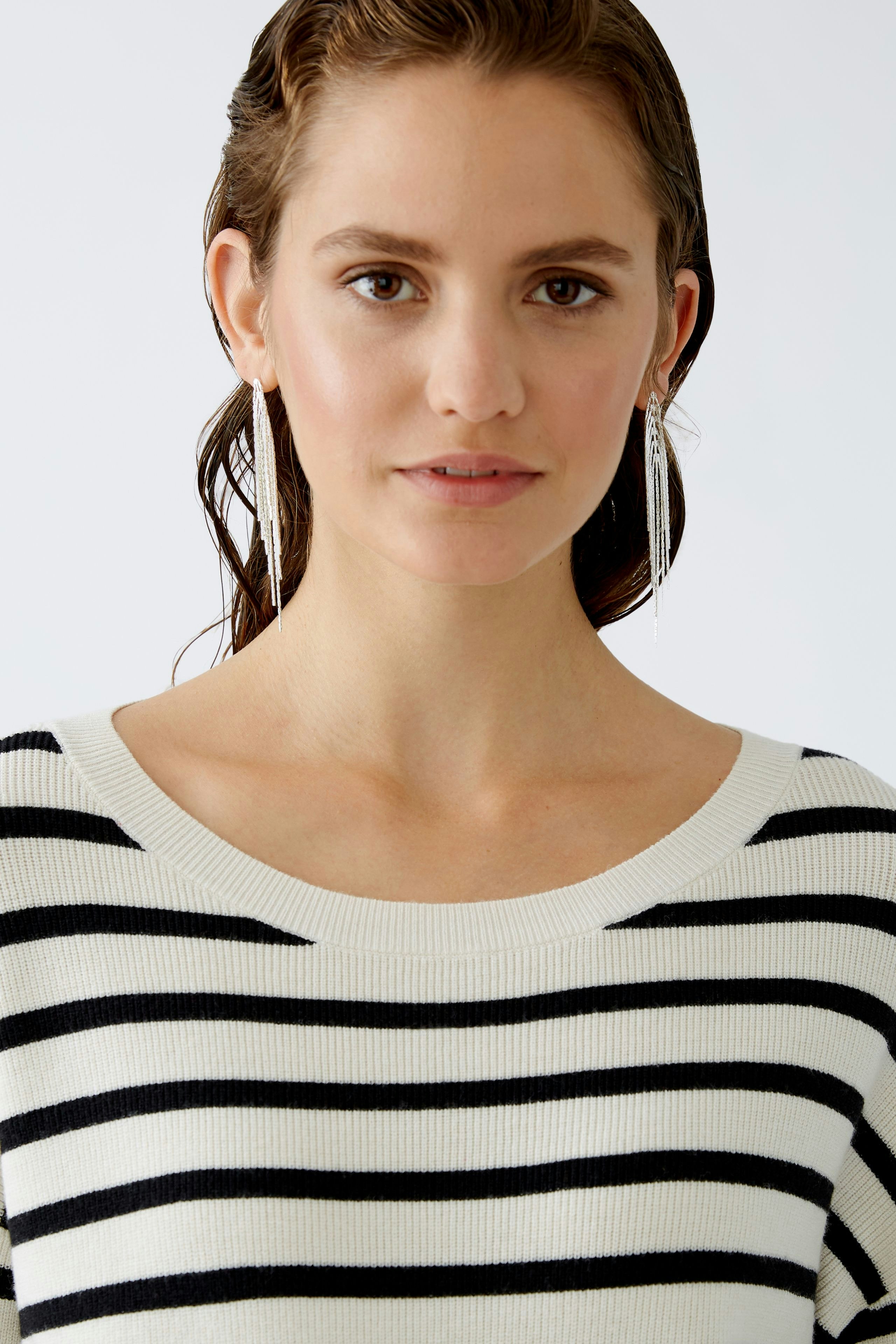 Modern women's pullover: A woman in a striped pullover with a relaxed neckline and elegant earrings.