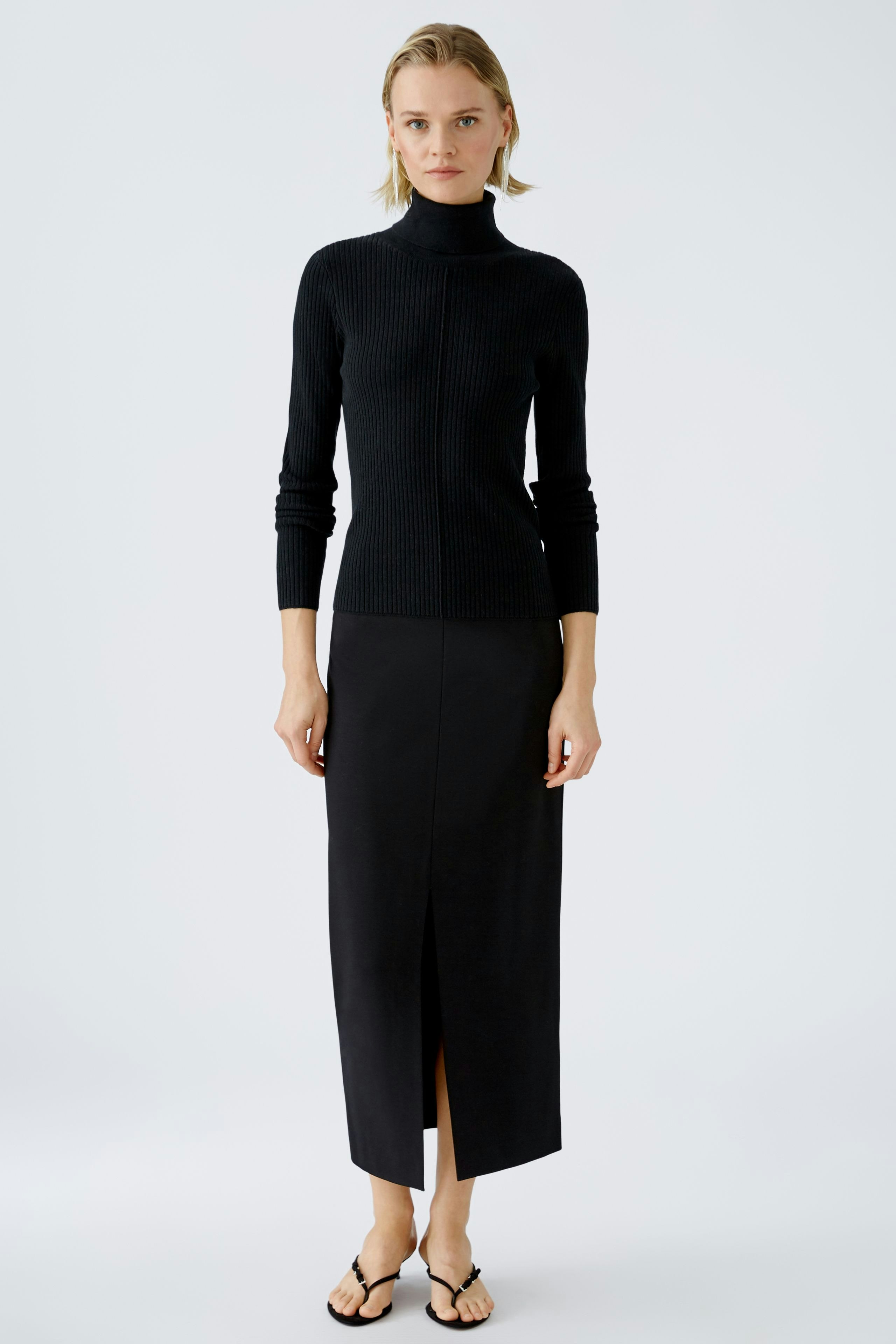 Elegant women's pullover: A woman in a black ribbed pullover with a high neck, paired with a sleek skirt.