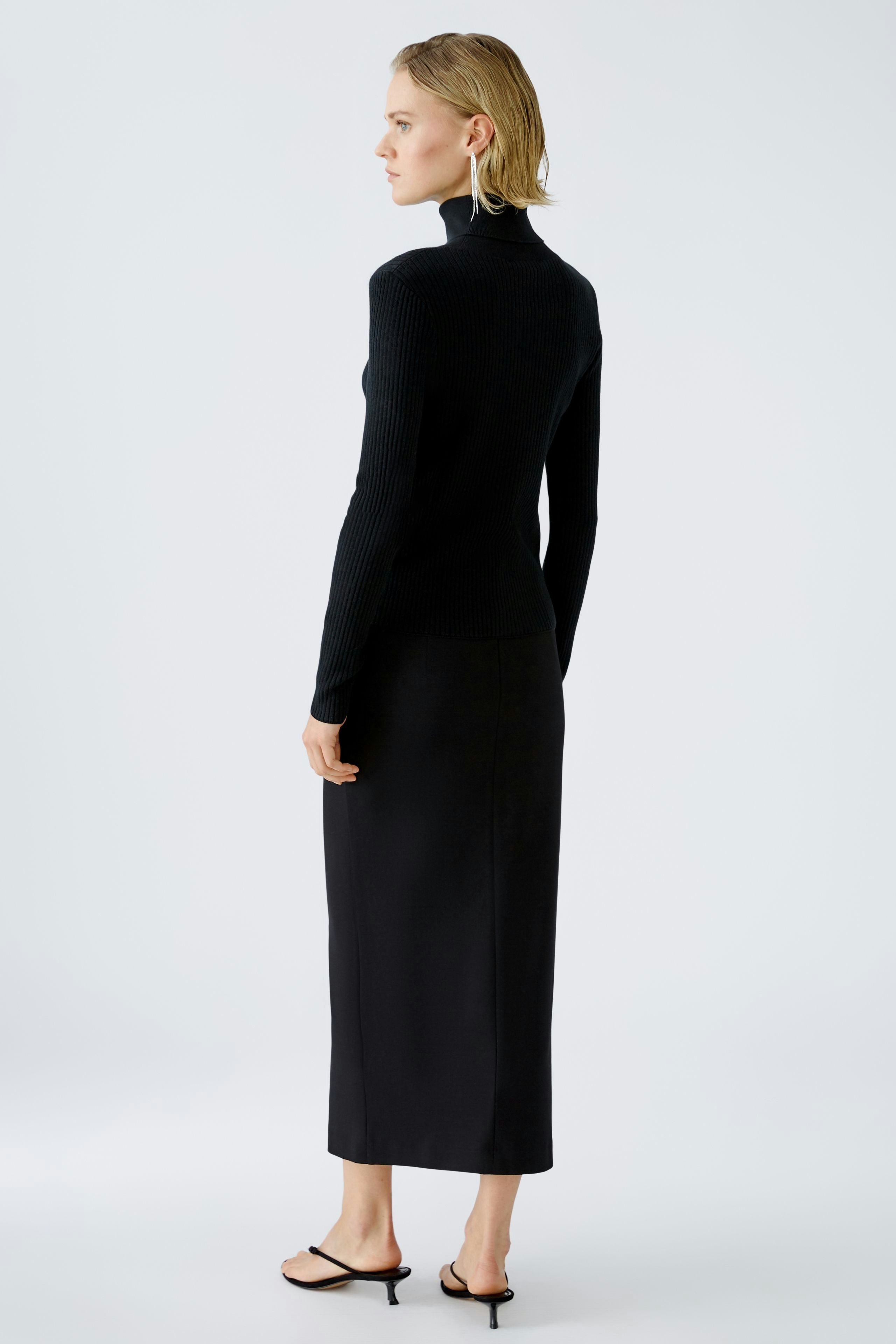 Elegant women's pullover: A woman in a fitted black ribbed pullover, showcasing a sleek silhouette.