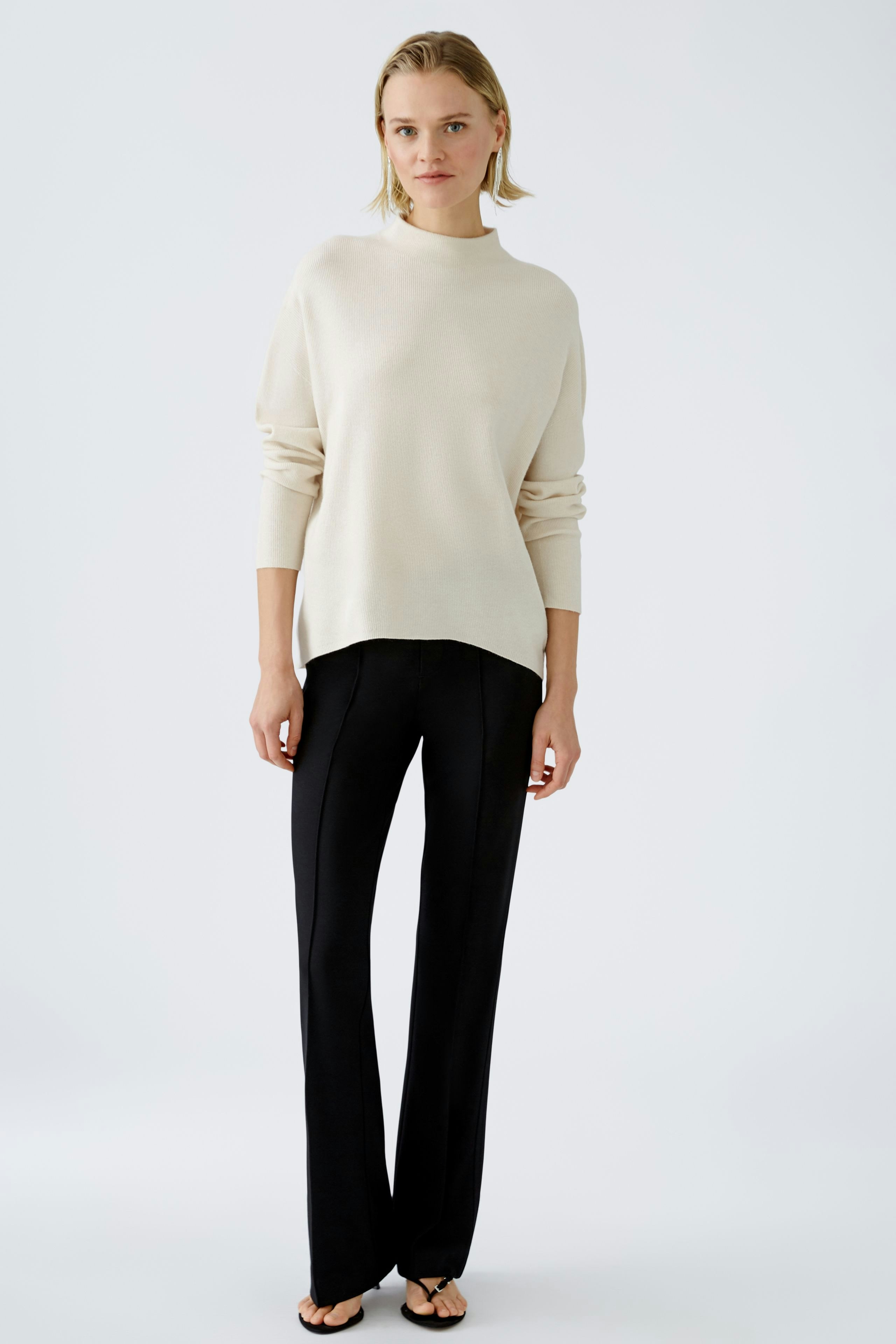 Modern women's pullover: A woman in a cream pullover paired with black trousers stands confidently.