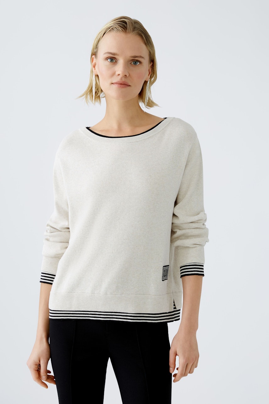 Modern women's pullover: A woman in a light beige pullover with black stripes looks confidently at the camera.