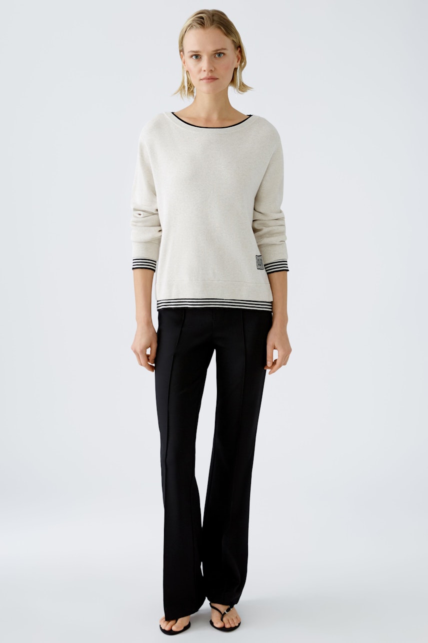 Modern women's pullover: A woman in a light pullover with striped details and black pants stands confidently.