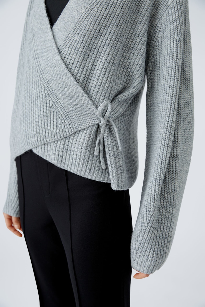 Stylish women's cardigan: A woman in a gray wrap cardigan with a tie detail, paired with sleek black pants.