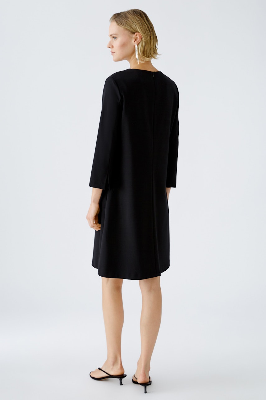 Elegant A-line dress: Woman in a sleek black dress with three-quarter sleeves, showcasing a timeless silhouette.