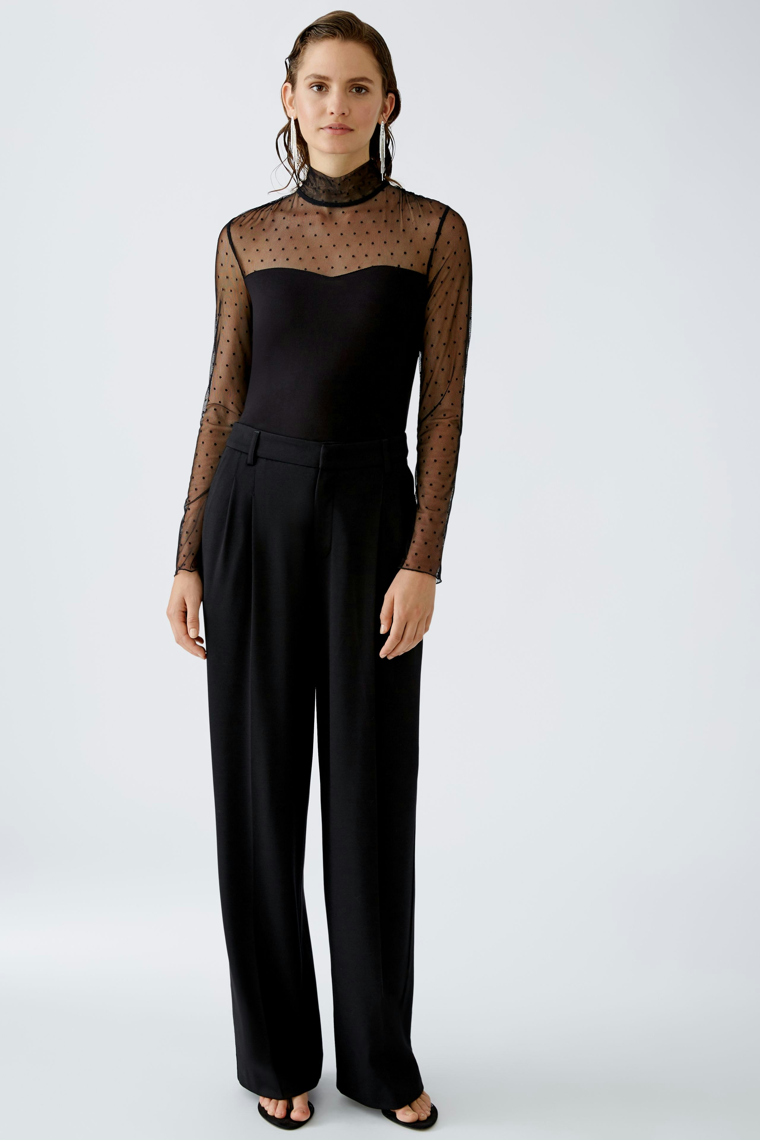 Elegantes Langarmshirt: Frau in schwarzem, transparentem Shirt mit Punkten und hohem Kragen.