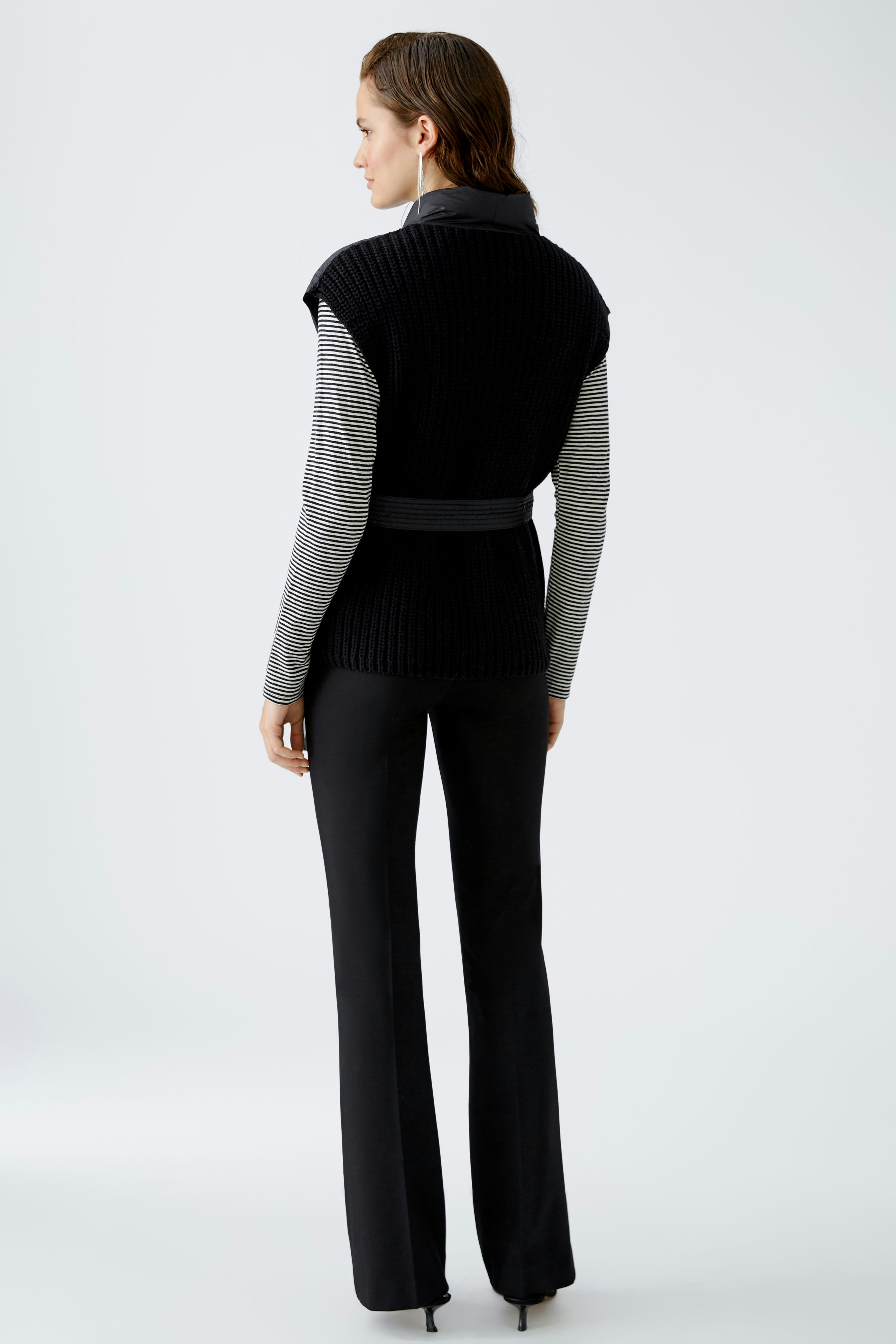 Stylish women's cardigan: A woman in a black knitted cardigan with a belt, paired with sleek trousers.