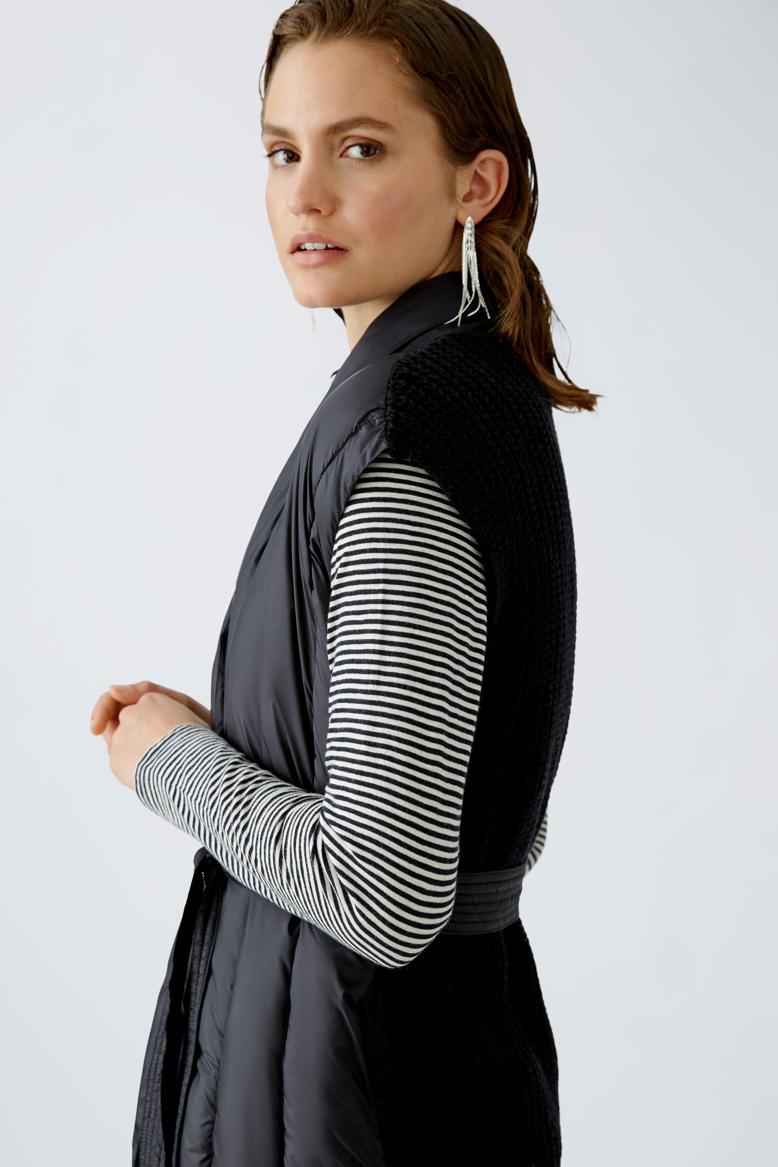 Stylish women's cardigan: A woman in a black knitted vest over a striped pullover, exuding elegance.