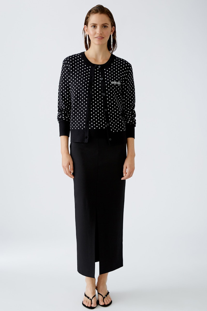 Stylish women's cardigan: A woman in a black cardigan with white dots and a sleek black skirt.