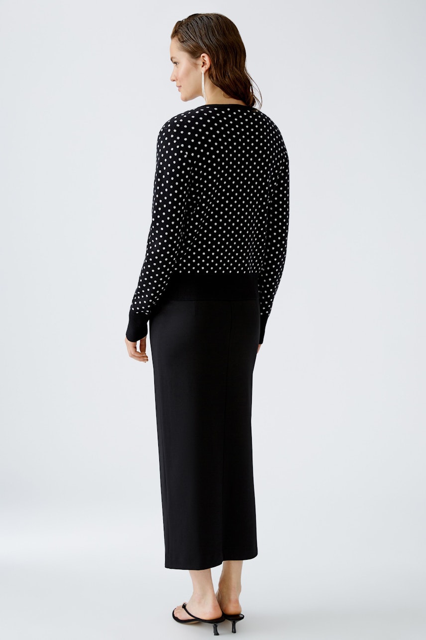 Stylish women's cardigan: A woman in a black polka dot cardigan and long skirt poses elegantly.