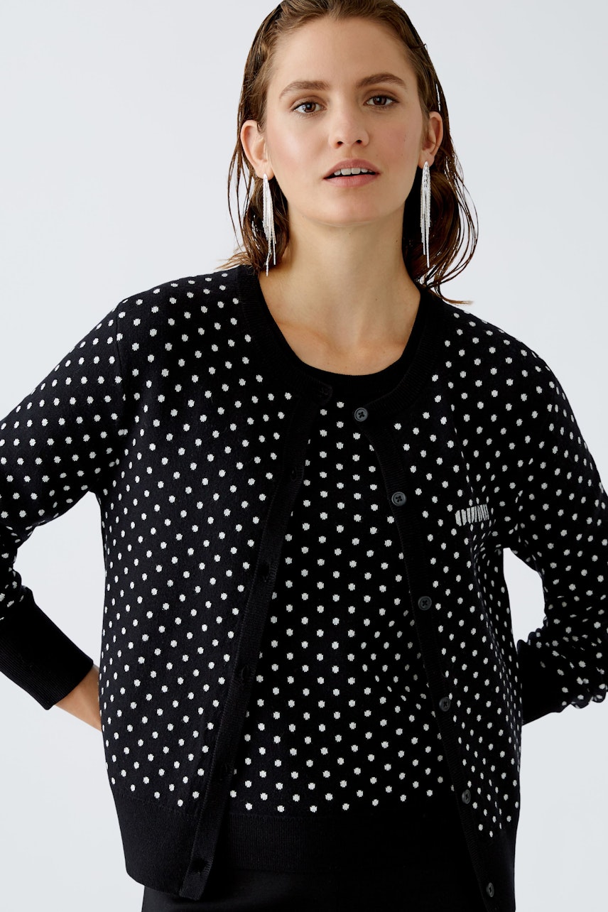 Stylish women's cardigan: A woman in a black polka dot cardigan looks confidently at the camera.