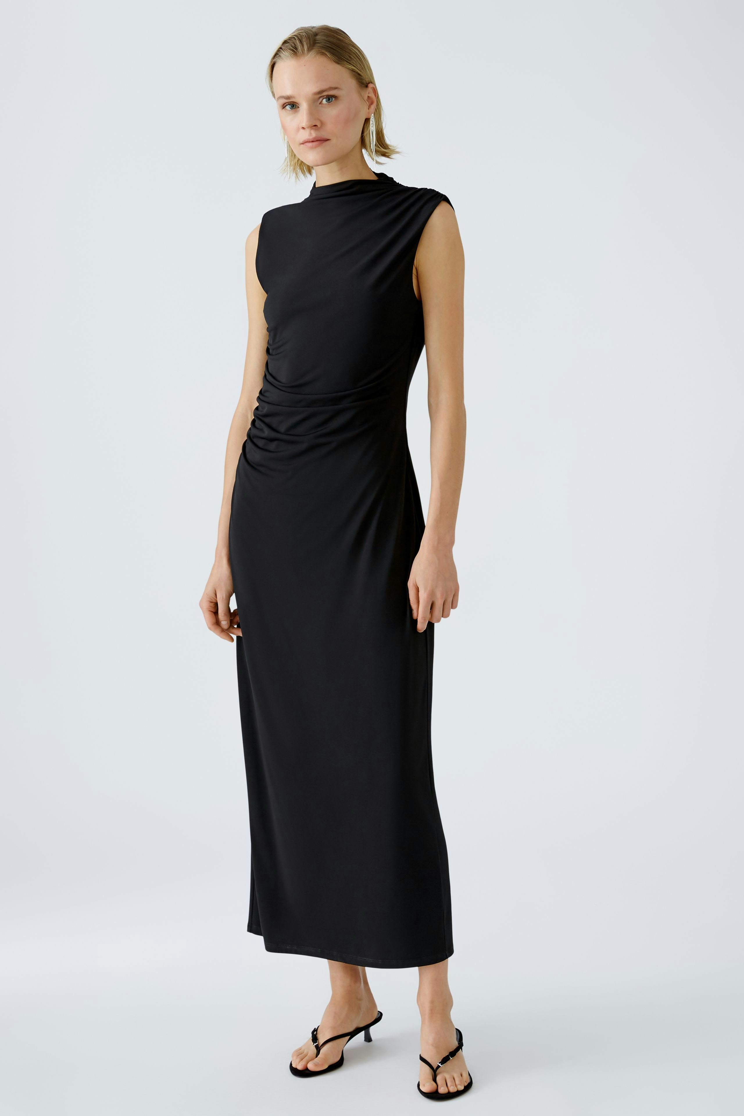 Elegantes Abendkleid: Frau in schwarzem, figurbetontem Kleid mit schlichten Details steht stilvoll.