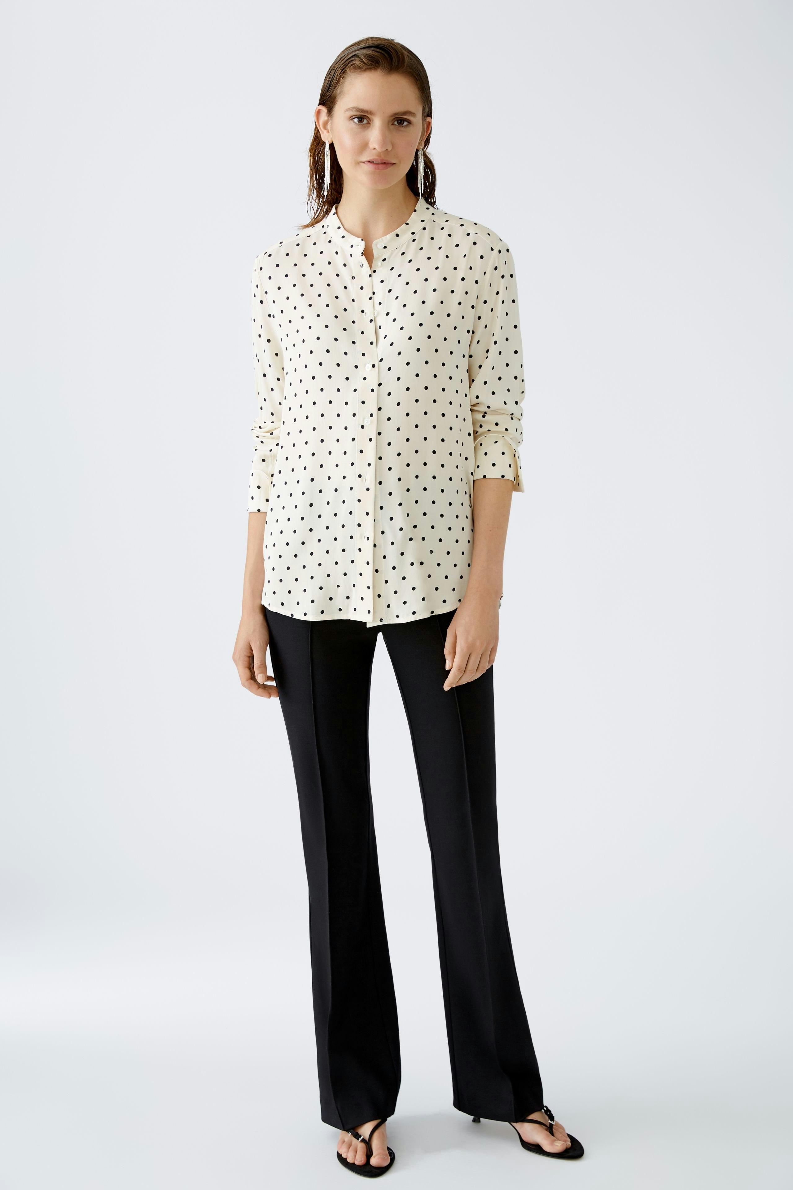 Chic women's blouse: A woman in a polka dot blouse with a relaxed fit, paired with sleek black pants.