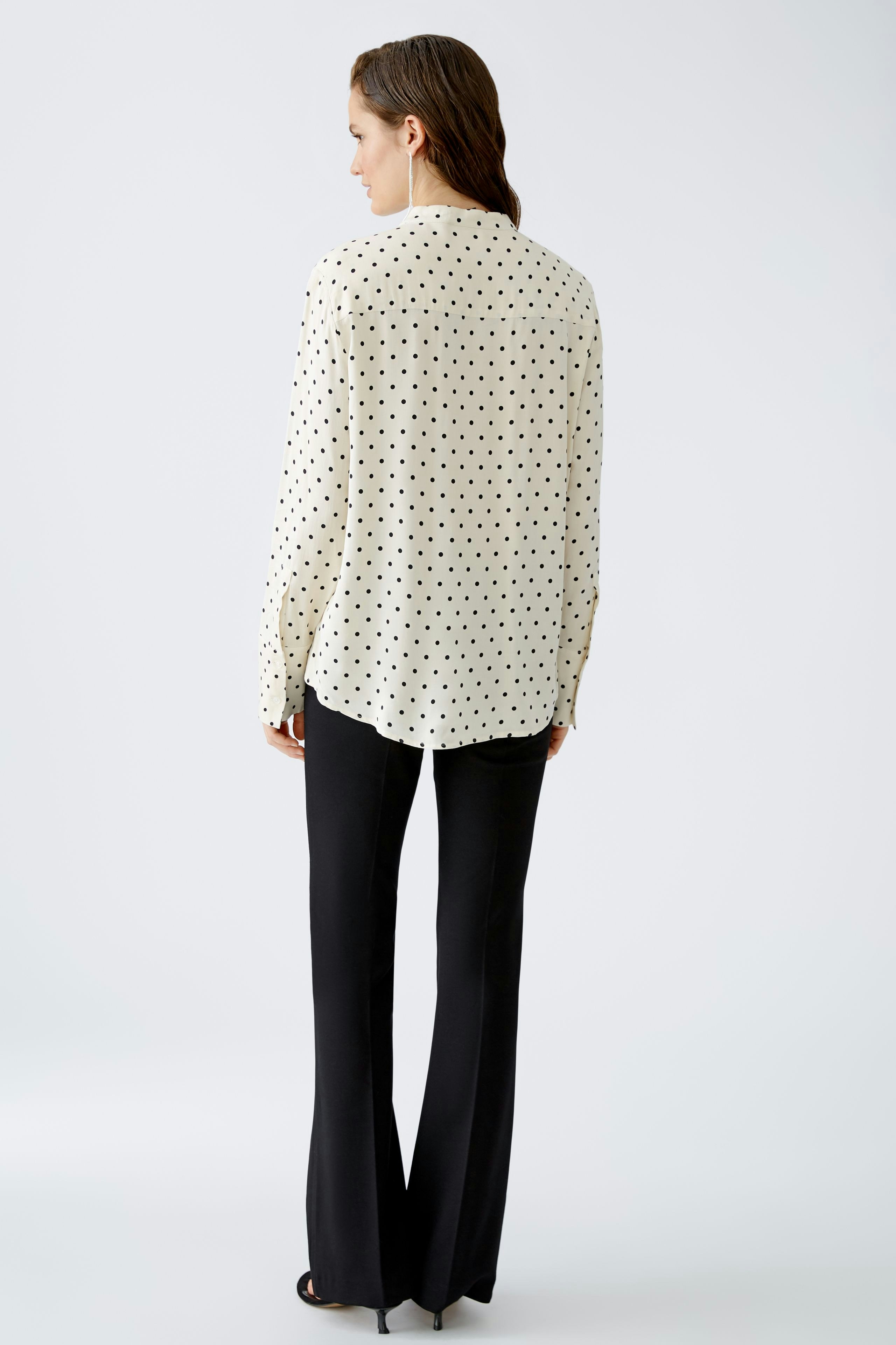 Elegant women's blouse: A woman in a polka dot blouse paired with black pants, showcasing a chic look.