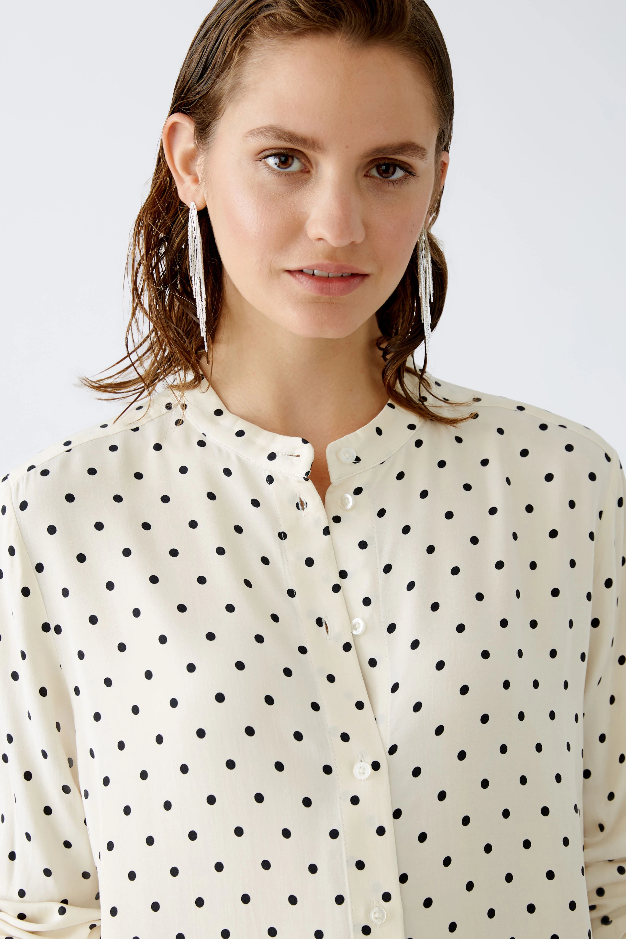 Elegant blouse: Woman in a cream blouse with black polka dots, featuring a button-up design.