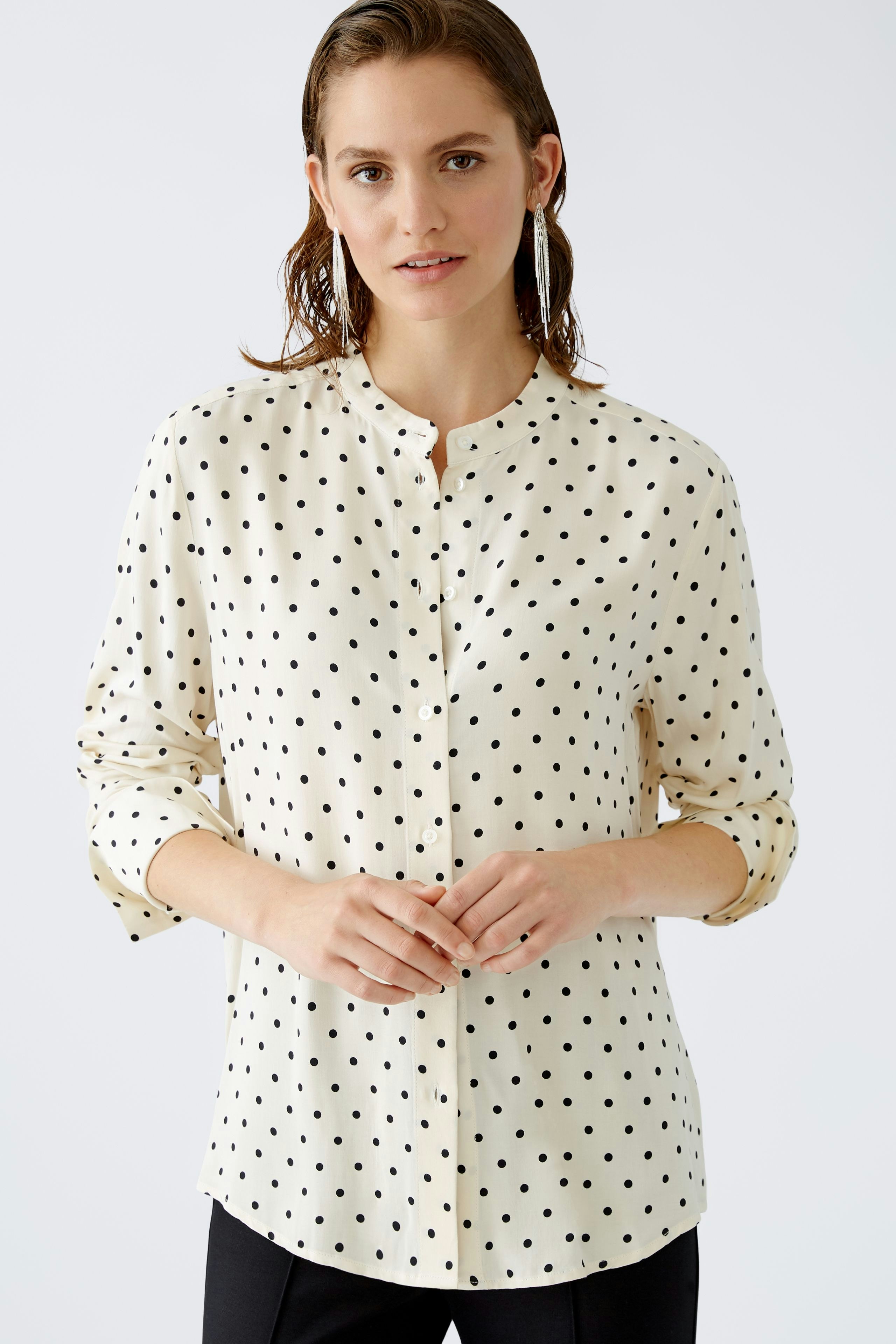 Elegant women's blouse: A woman in a cream blouse with black polka dots stands confidently.