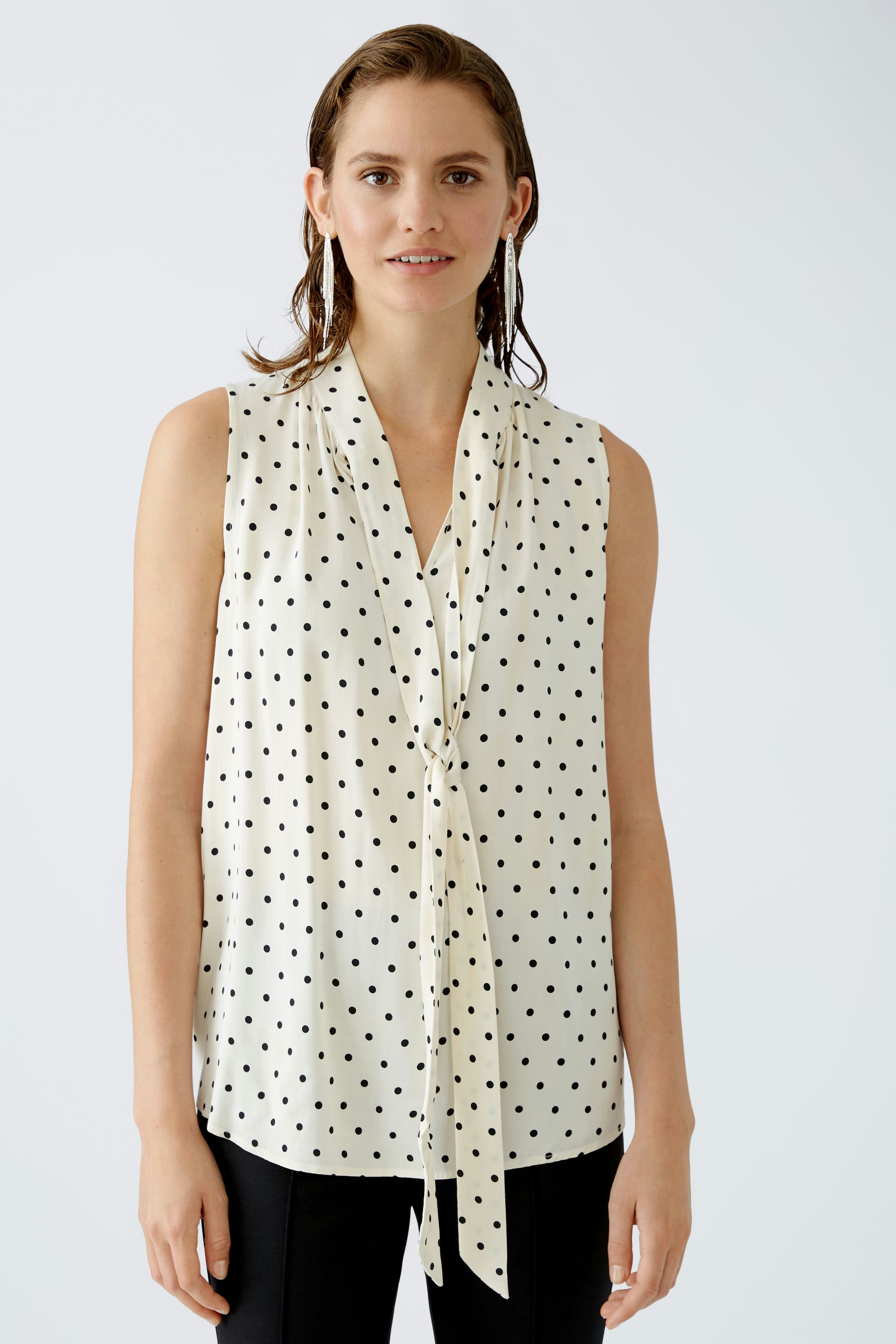 Elegant women's blouse: A woman in a sleeveless, polka dot blouse with a stylish tie detail.
