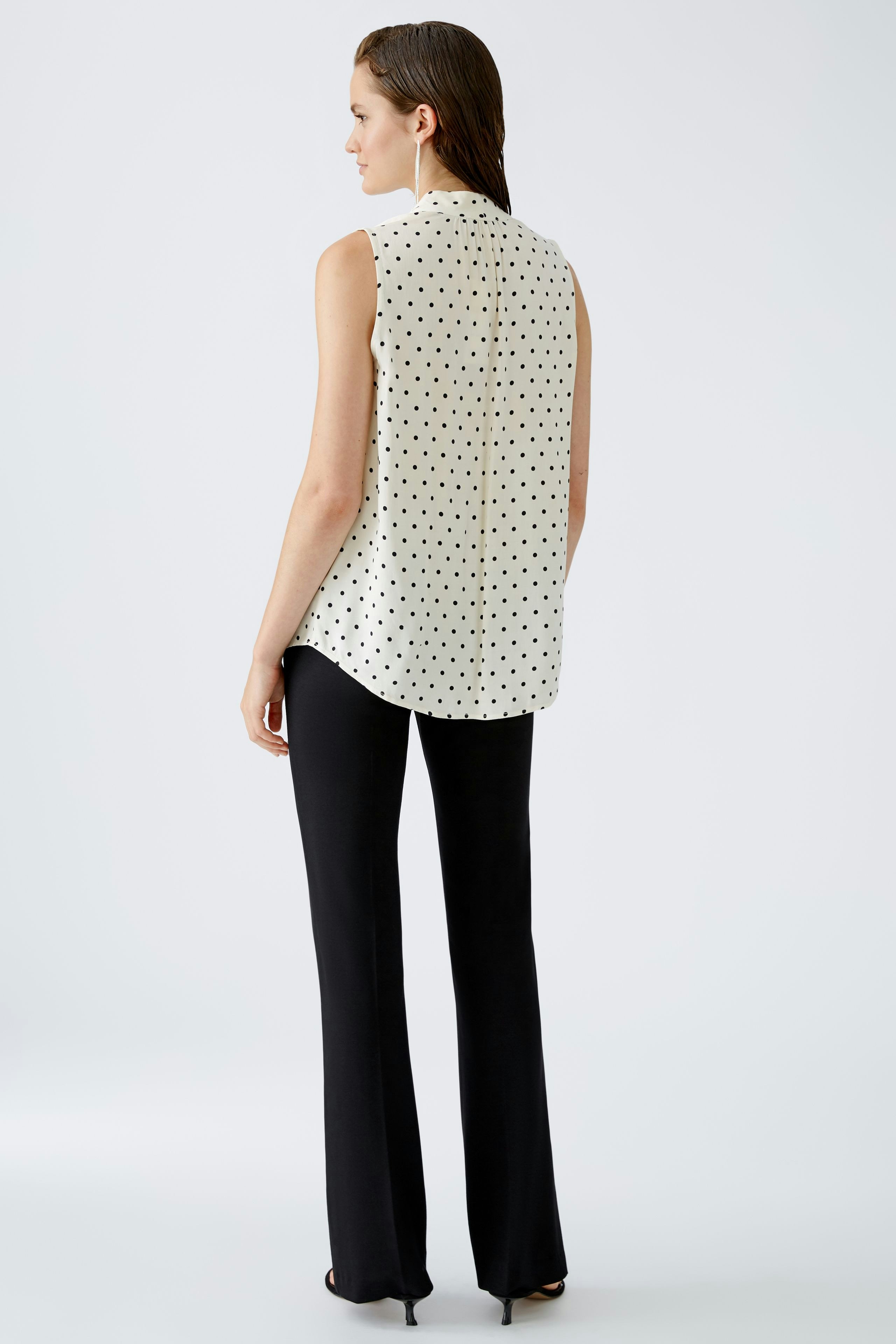 Stylish women's blouse: A woman in a sleeveless polka dot blouse paired with black pants.