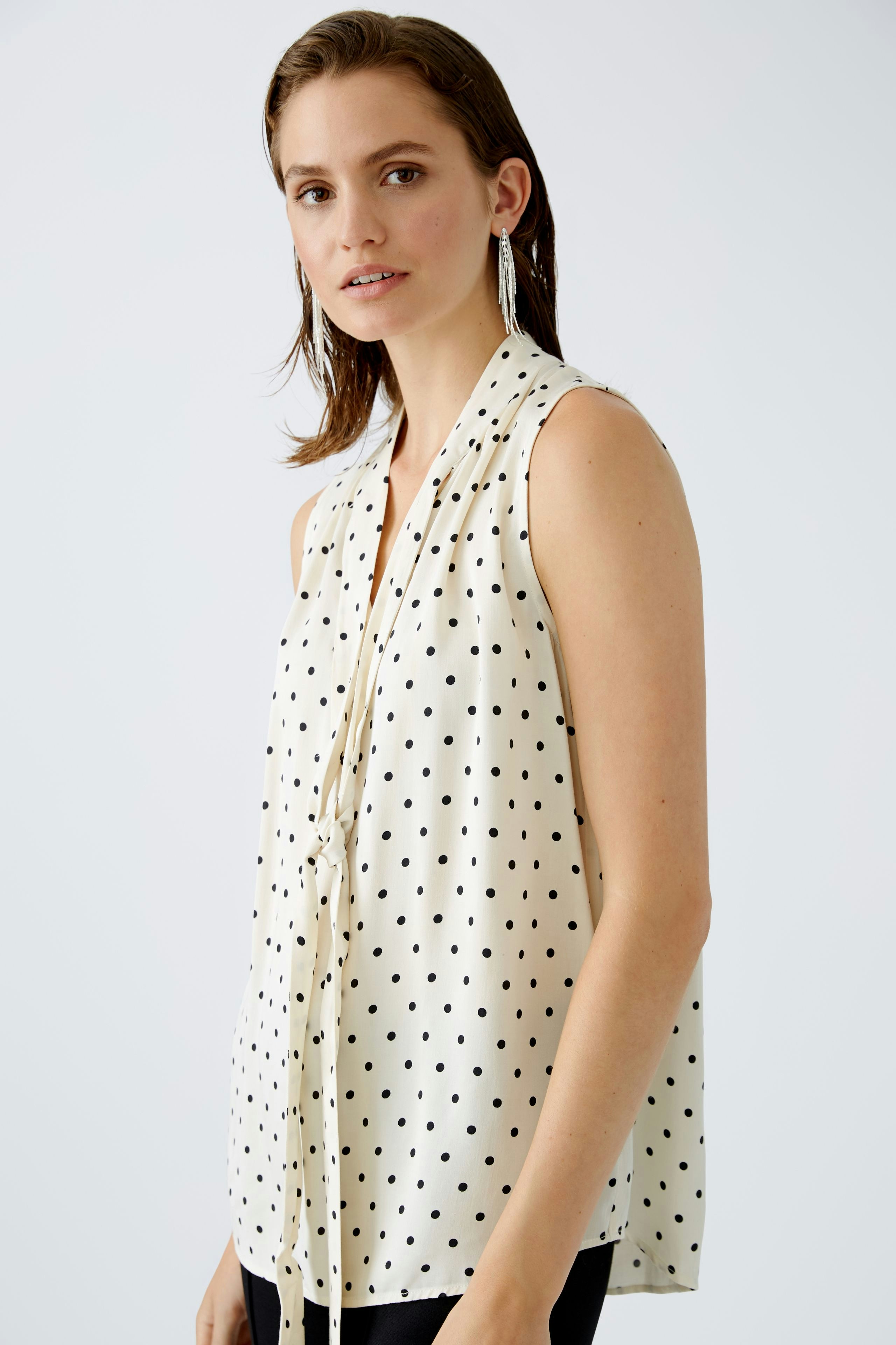 Elegant women's blouse: A woman in a sleeveless, polka dot blouse with a stylish tie detail.