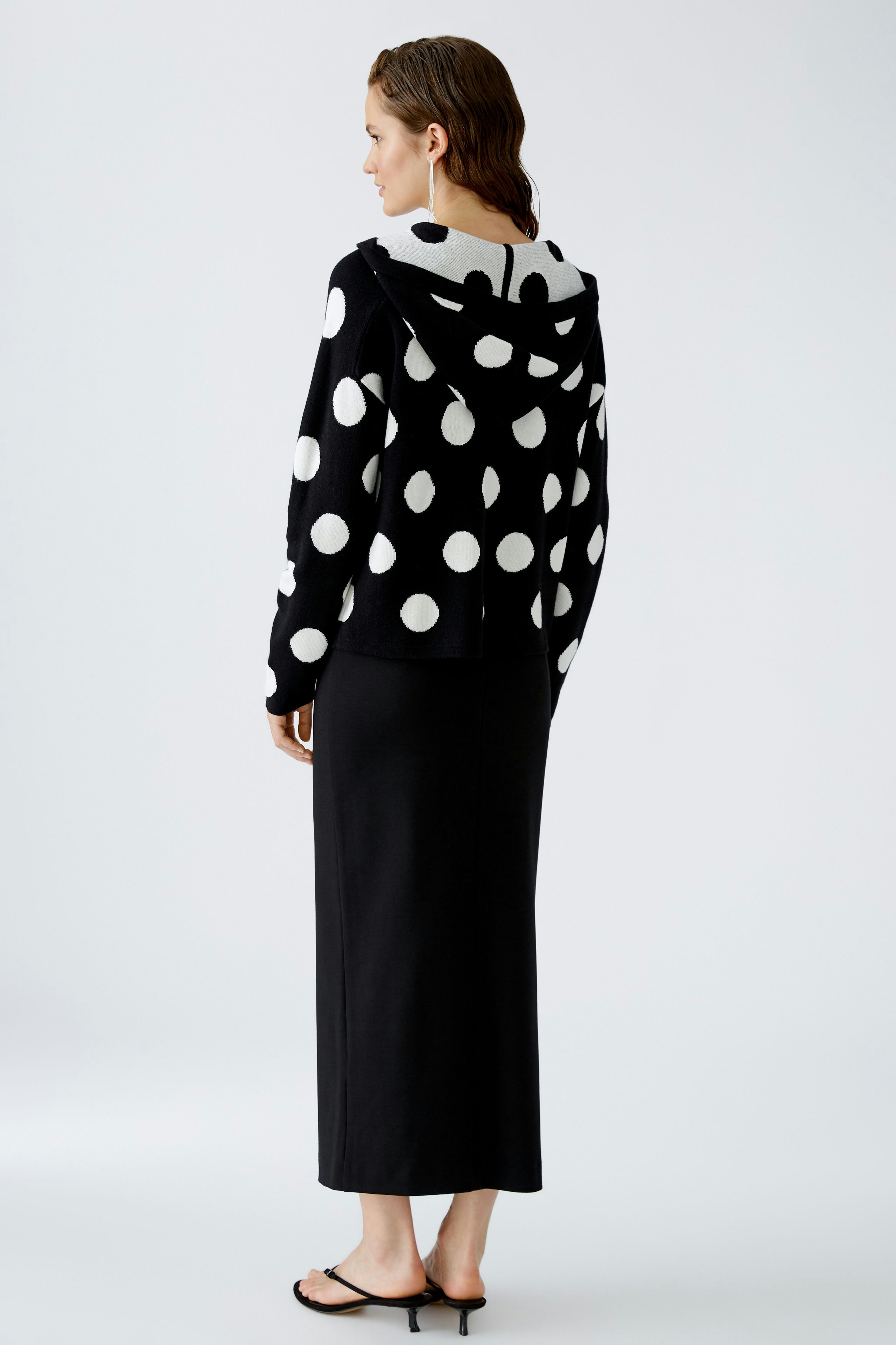 Stylish women's pullover: A woman in a black and white polka dot hoodie, paired with a sleek black skirt.
