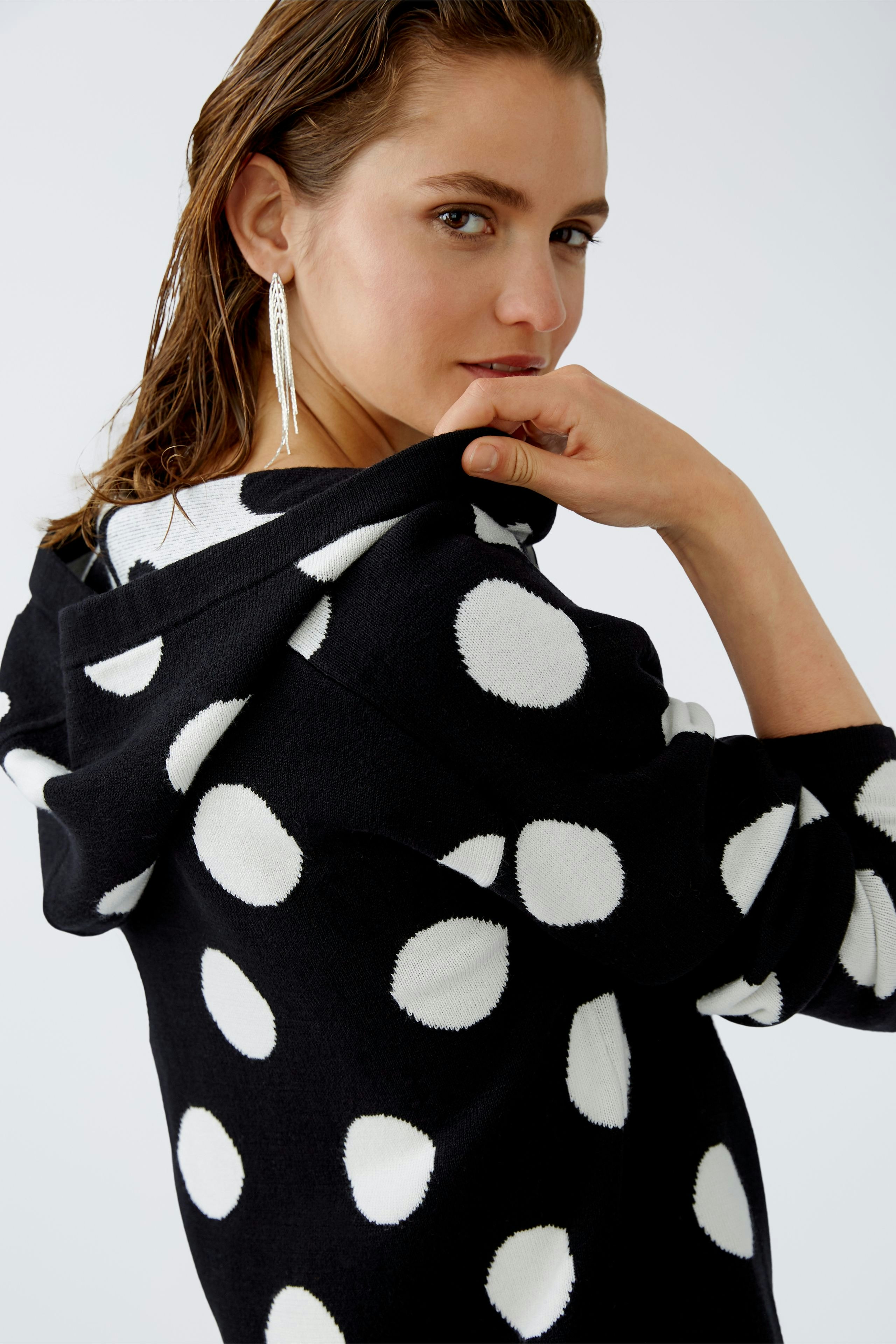 Stylish women's pullover: Woman in a black hoodie with white polka dots, exuding confidence.