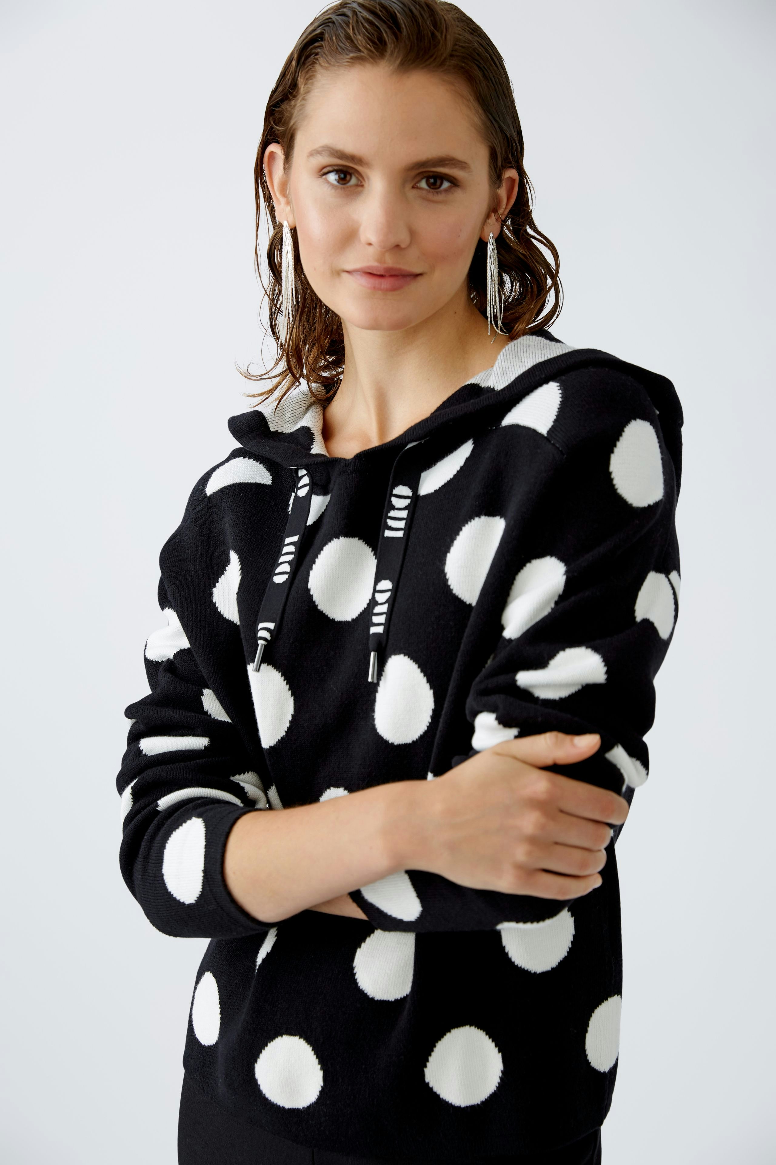 Stylish women's pullover: A woman in a black hoodie with white polka dots poses confidently.